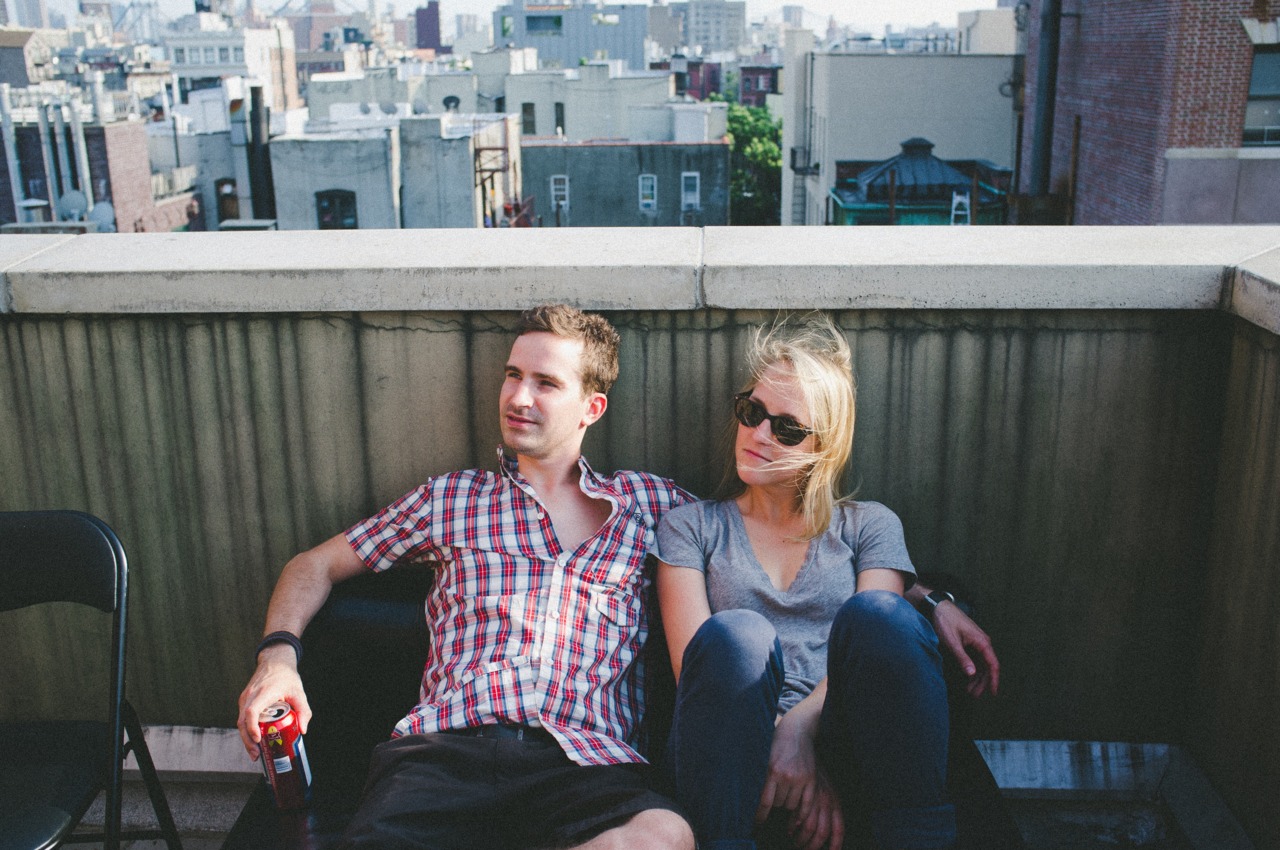 Couple relaxing together on a rooftop bench against the parapet wall overlooking the city skyline.