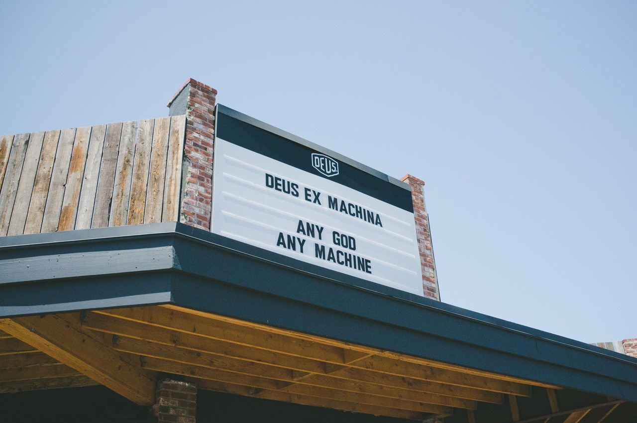 Exterior marquee sign against a clear blue sky reading 'Deus Ex Machina / Any God Any Machine' in Venice, California, captured with a Fujifilm FinePix X100.