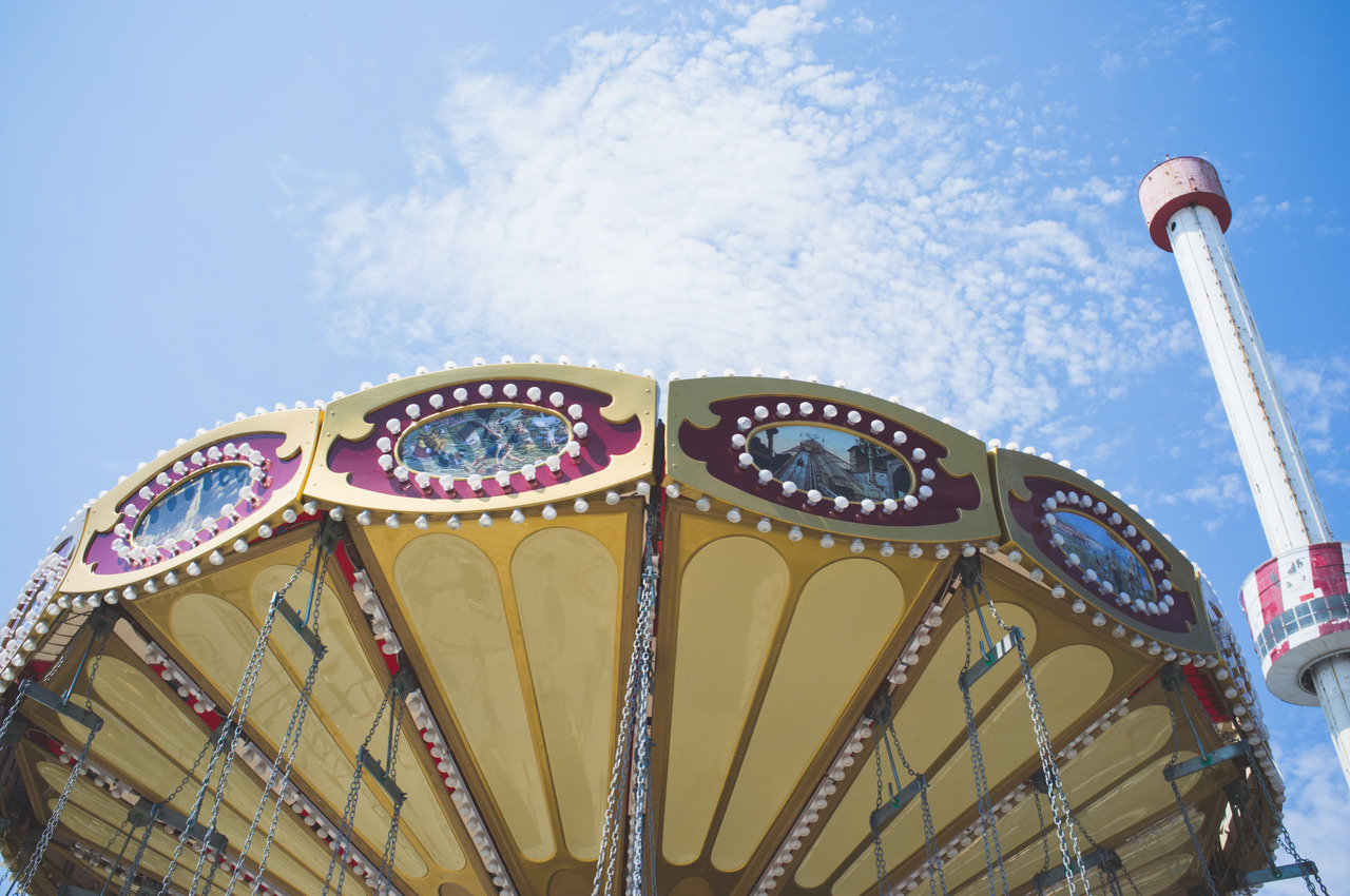 Colorful swing carousel ride with painted panels and hanging chains against a blue sky with wispy clouds.
