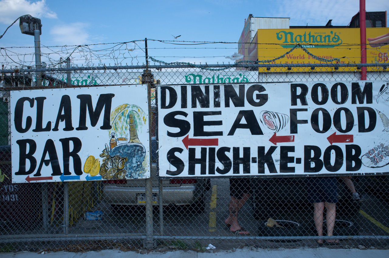 Signs for 'CLAM BAR' and 'DINING ROOM SEA FOOD SHISH-KE-BOB' outside Nathan's Famous in Coney Island.