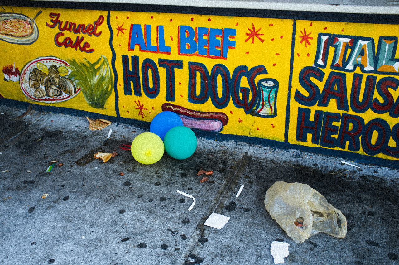 Food stand counter reading 'ALL BEEF HOT DOGS / ITALIAN SAUSAGE HEROS' with three balloons on the ground.