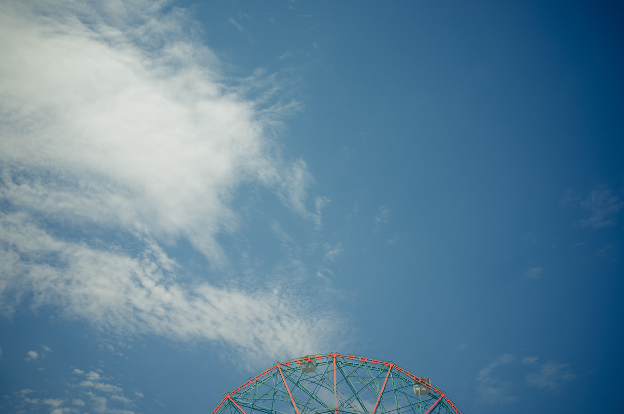 Top arc of Deno's Wonder Wheel Ferris wheel rising against a blue sky with soft white clouds.