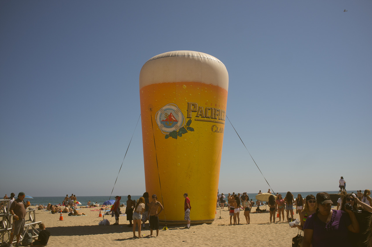 Giant inflatable Pacifico beer pint on sunny sand with beachgoers at the Huntington Beach US Open.