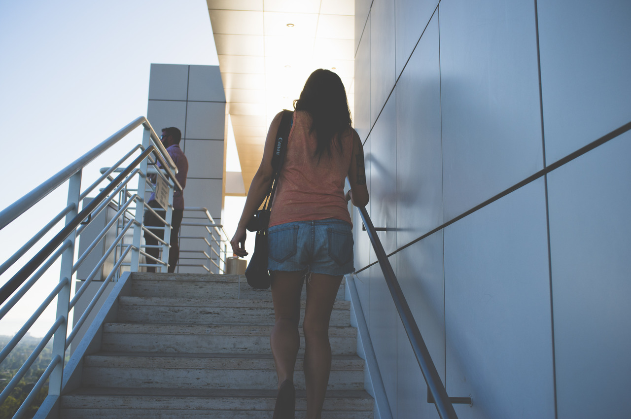 Carmen climbing an outdoor stone staircase with a camera slung over her shoulder at the Getty Center in Los Angeles, captured with a Fujifilm FinePix X100.