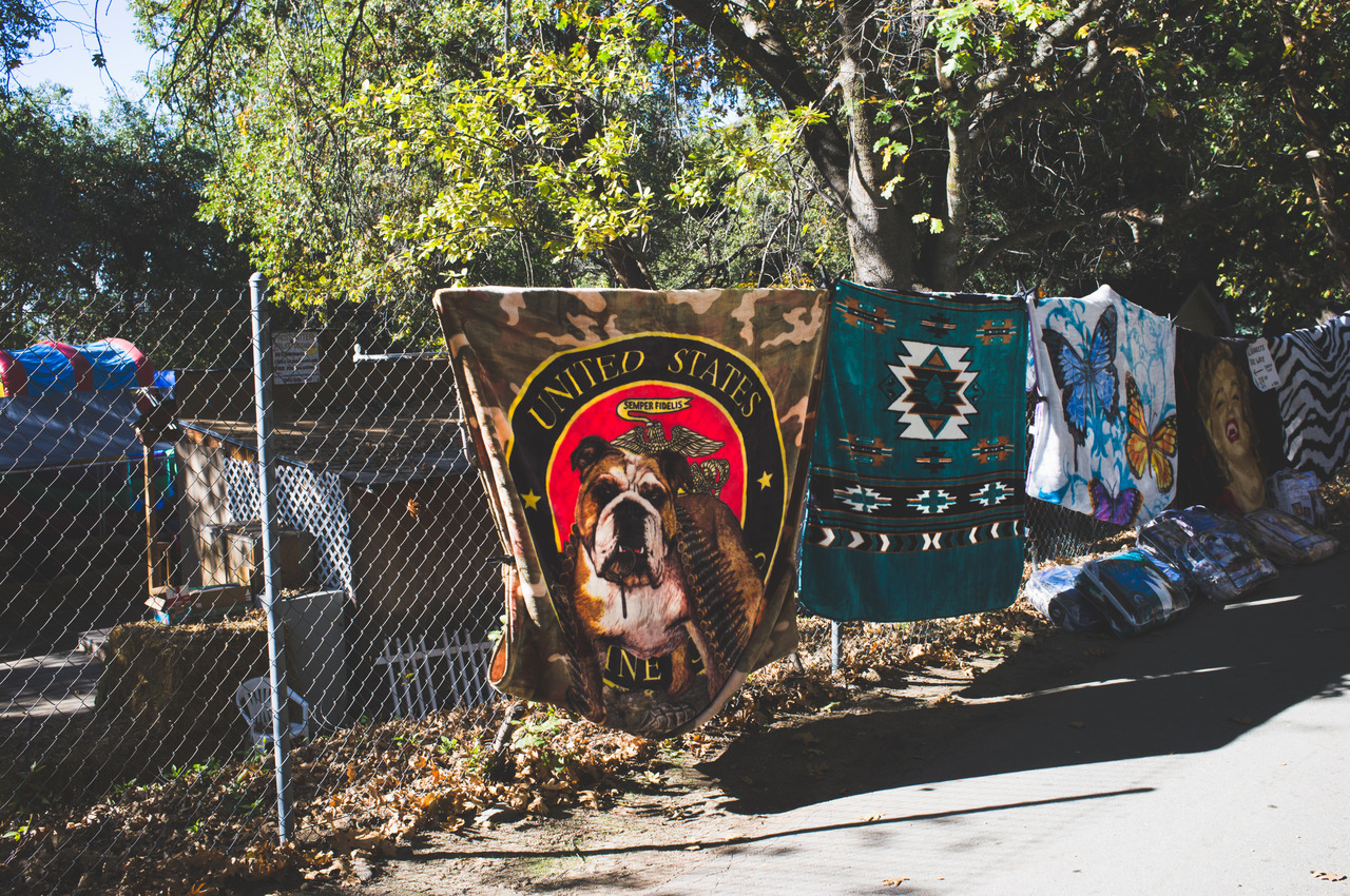 Fleece blankets including a US Marine Corps bulldog and Southwestern designs hanging for sale on a roadside fence in Oak Glen, captured with a Fujifilm FinePix X100.