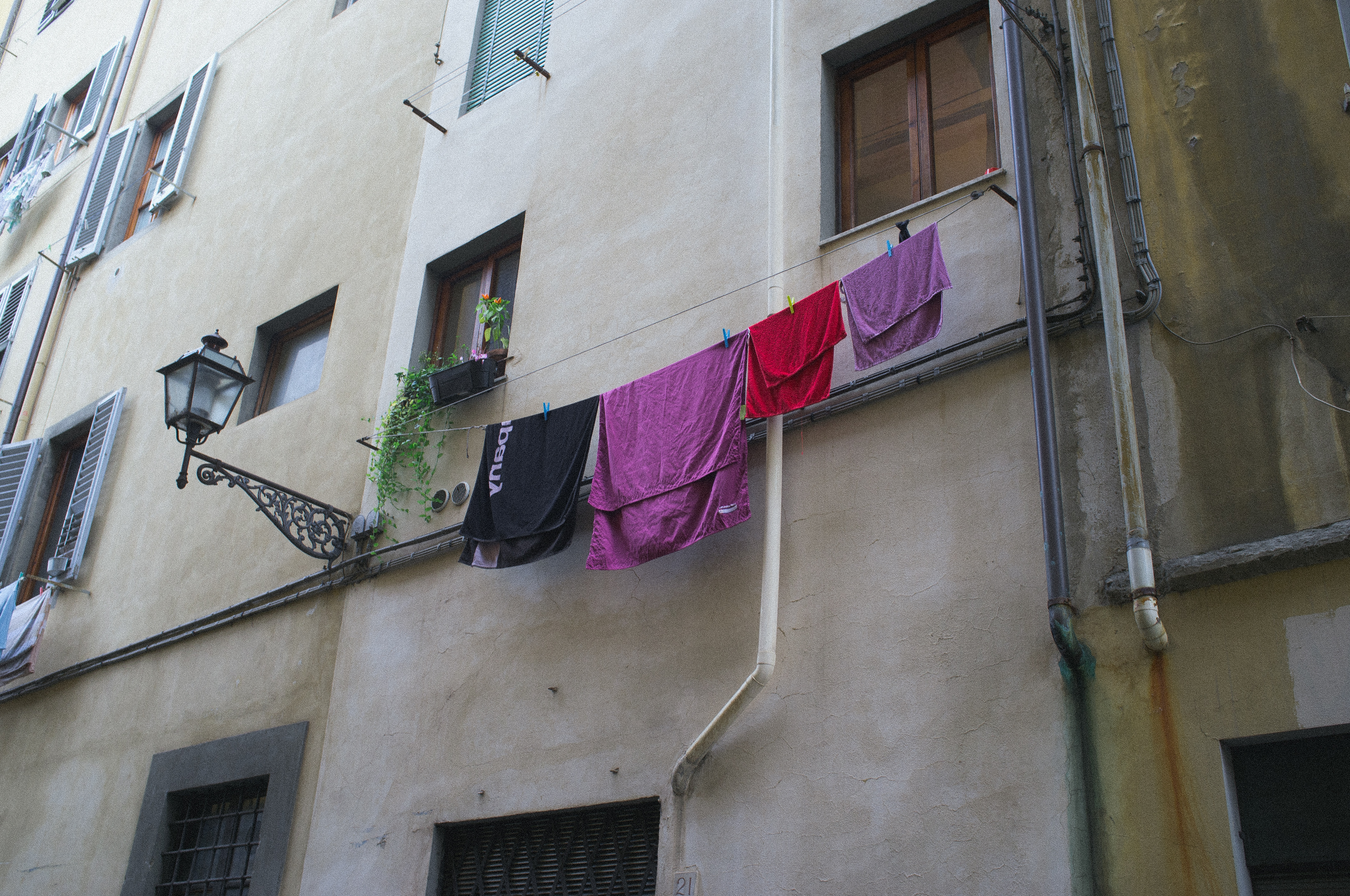 Narrow Florentine alleyway with colorful laundry hanging from a high clothesline beside a wrought-iron street lantern and shuttered windows, captured with a Fujifilm FinePix X100.