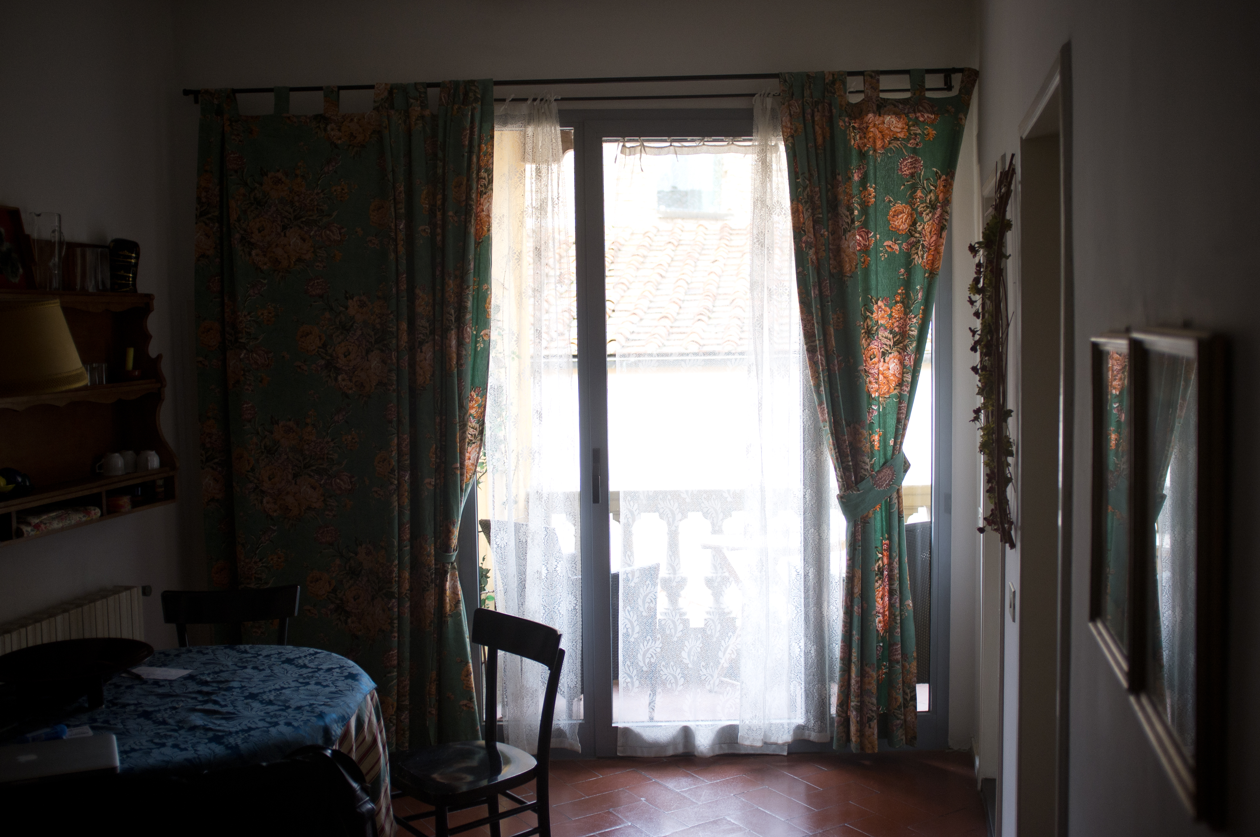 Interior view of an Italian apartment dining table by an open window looking out onto wet terracotta rooftops in Tuscany, captured with a Fujifilm FinePix X100.