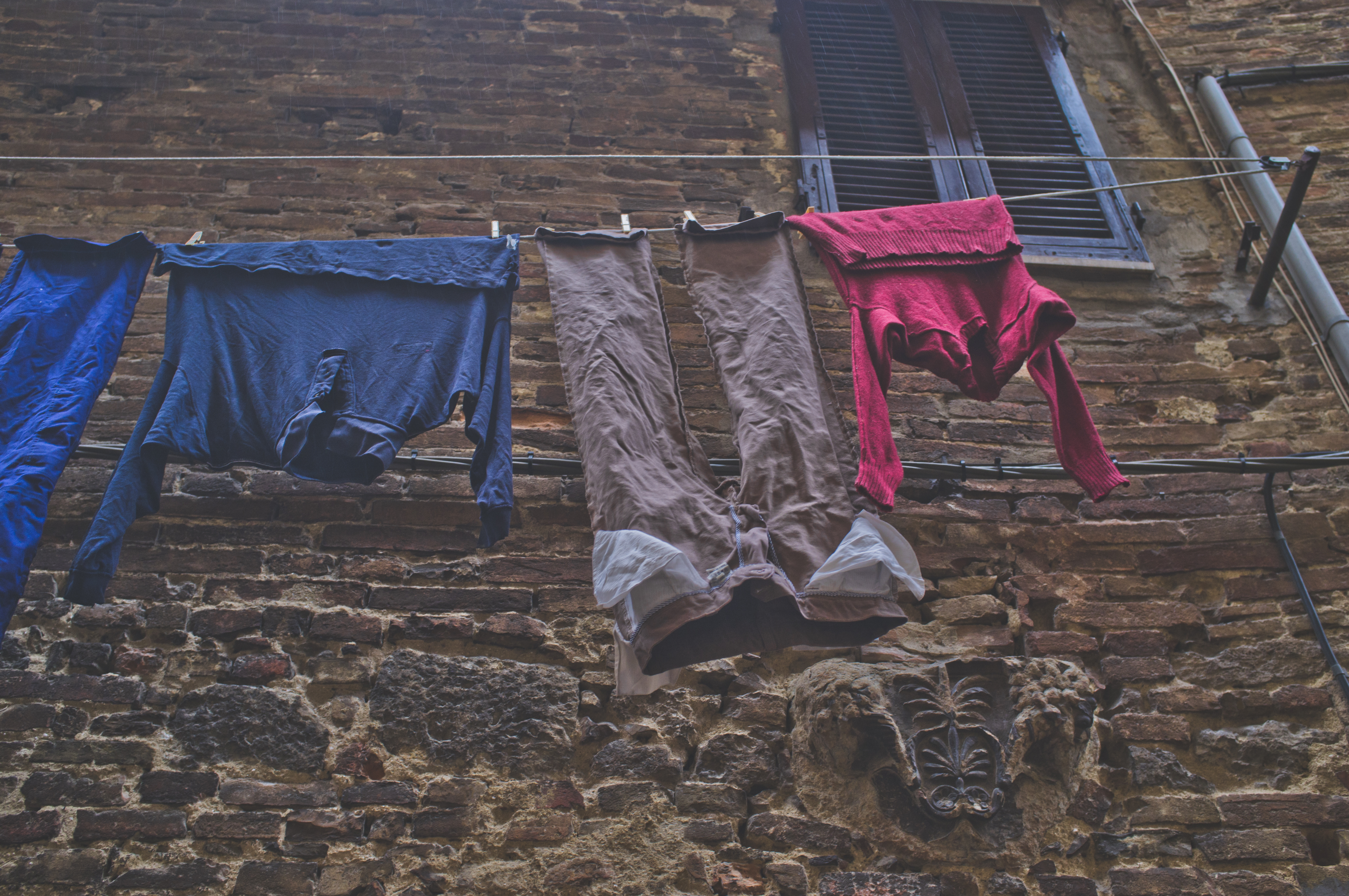 Clothes drying on an outdoor line against a weathered brick facade beside a carved classical stone relief in Florence, captured with a Fujifilm FinePix X100.