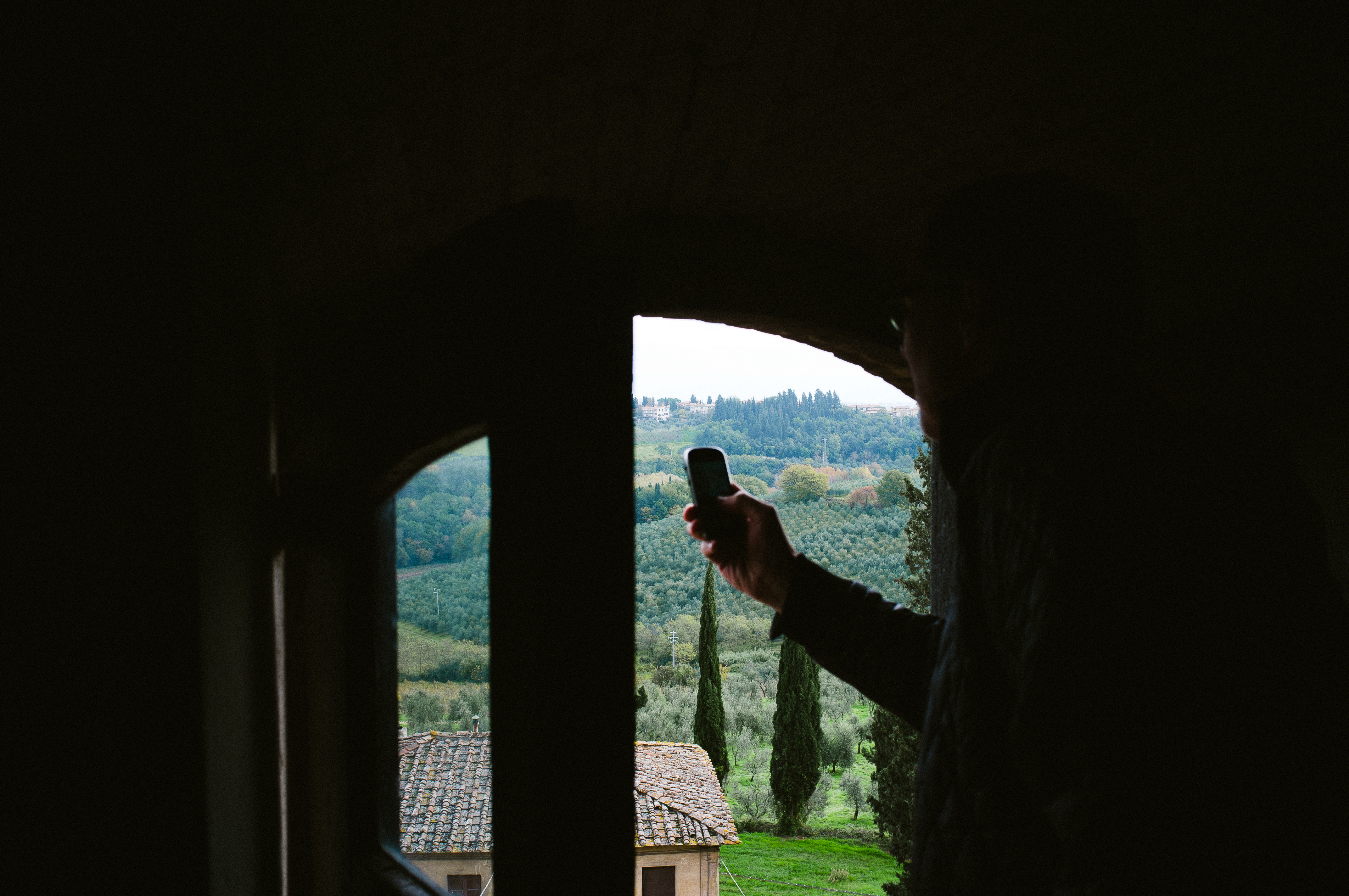 Person in an arched stone window looking out over the Tuscan countryside and olive groves.