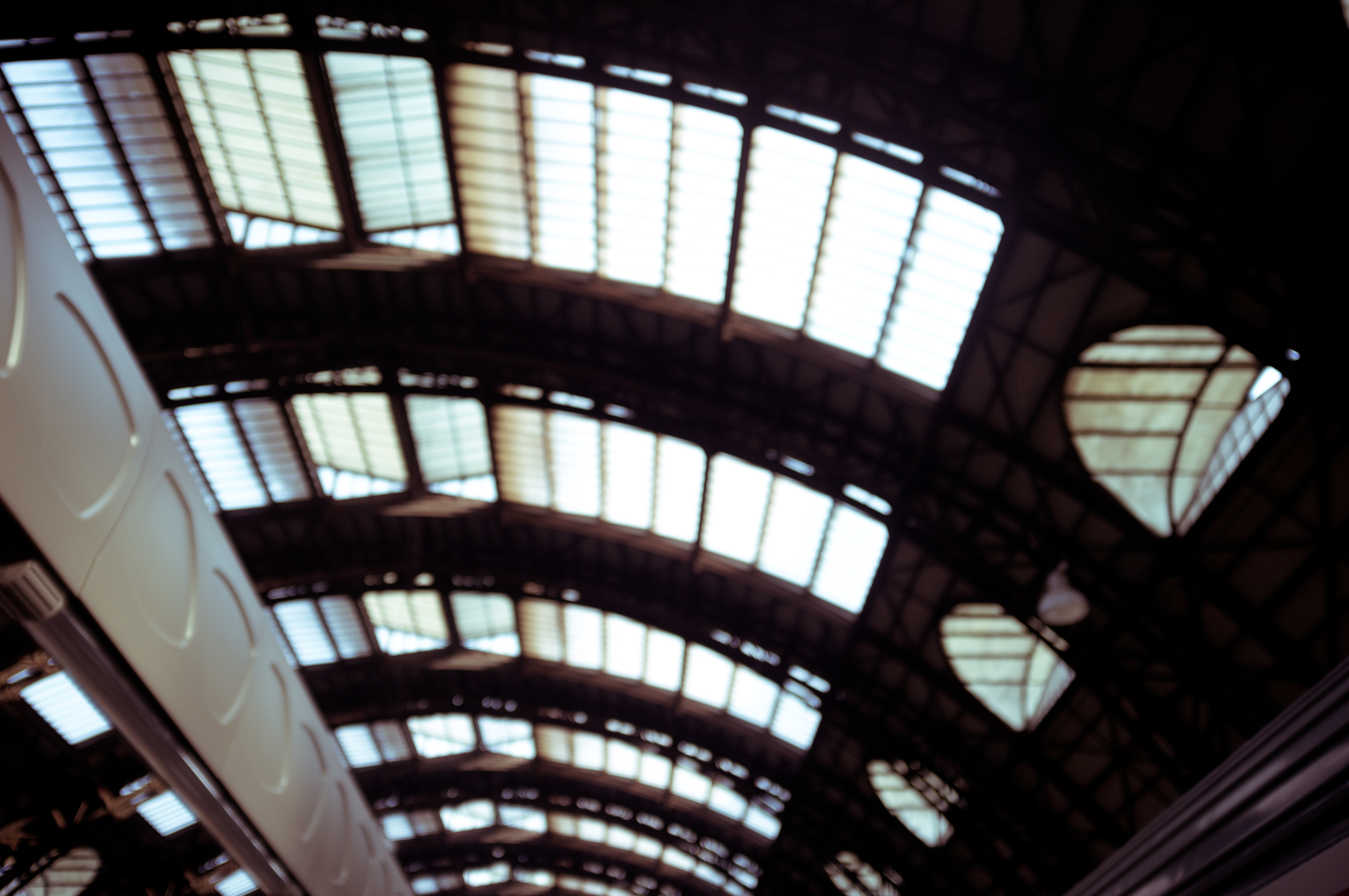 Atmospheric bokeh blur of the grand curved steel and glass arched ceiling canopy of a European train station.