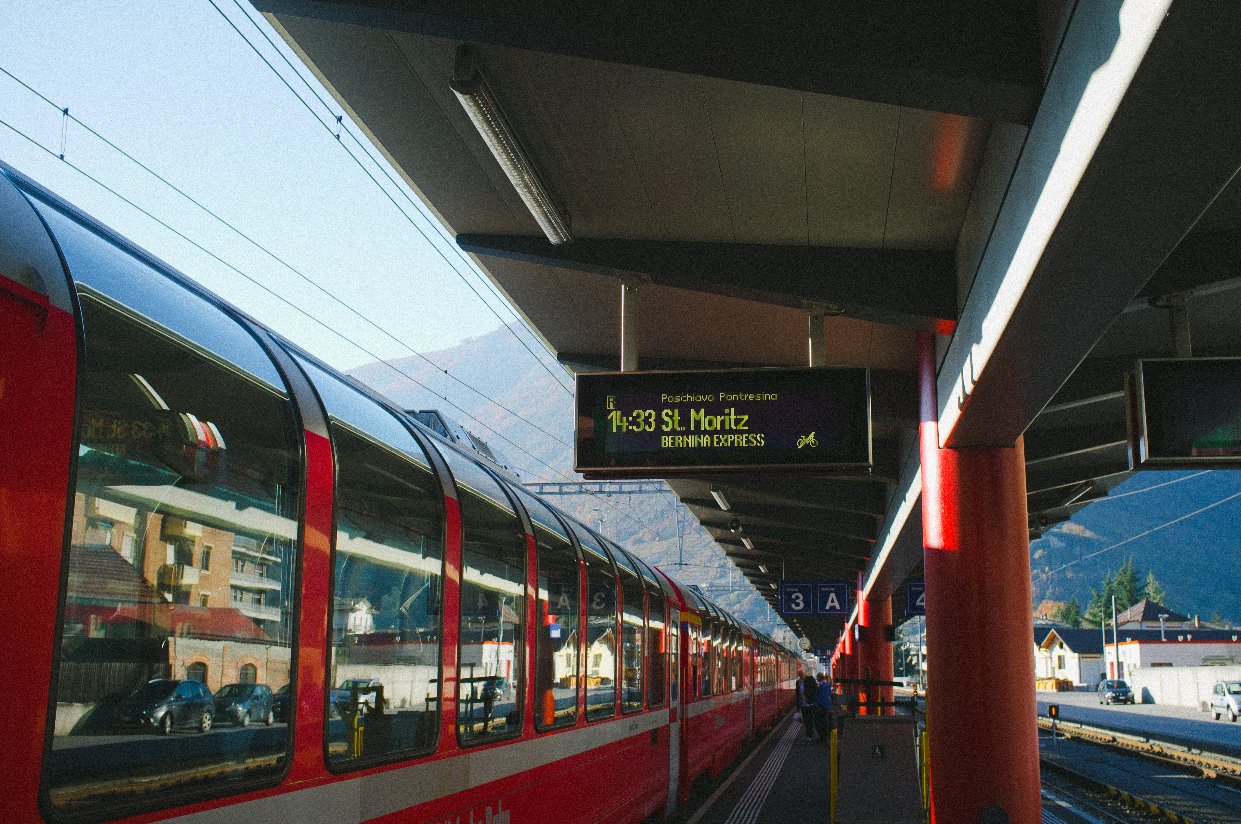 Departure board reading '14:33 St. Moritz BERNINA EXPRESS' beside a red Bernina Express train.