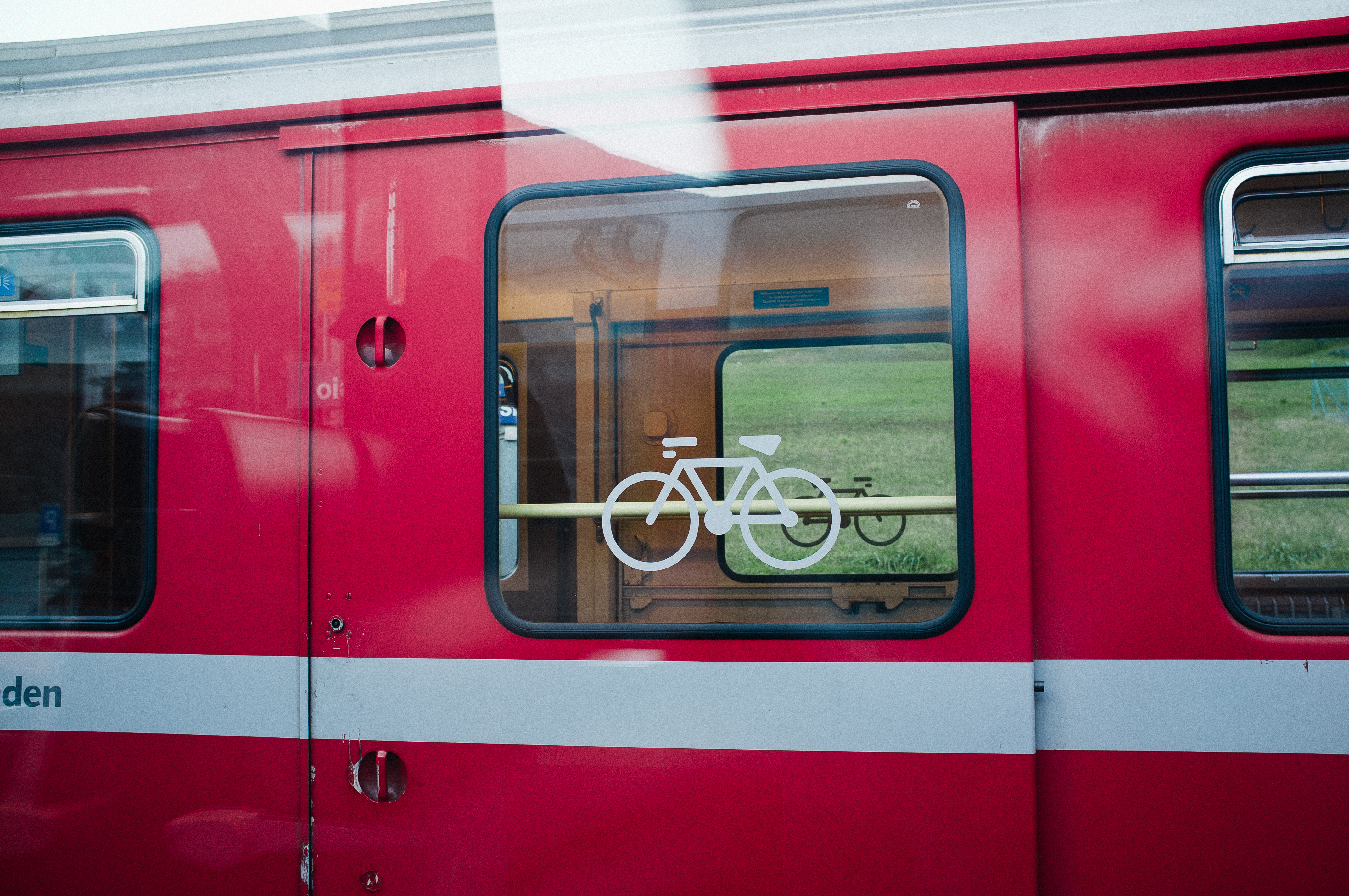 Red Swiss passenger train car exterior door featuring bicycle transport icon on glass window.
