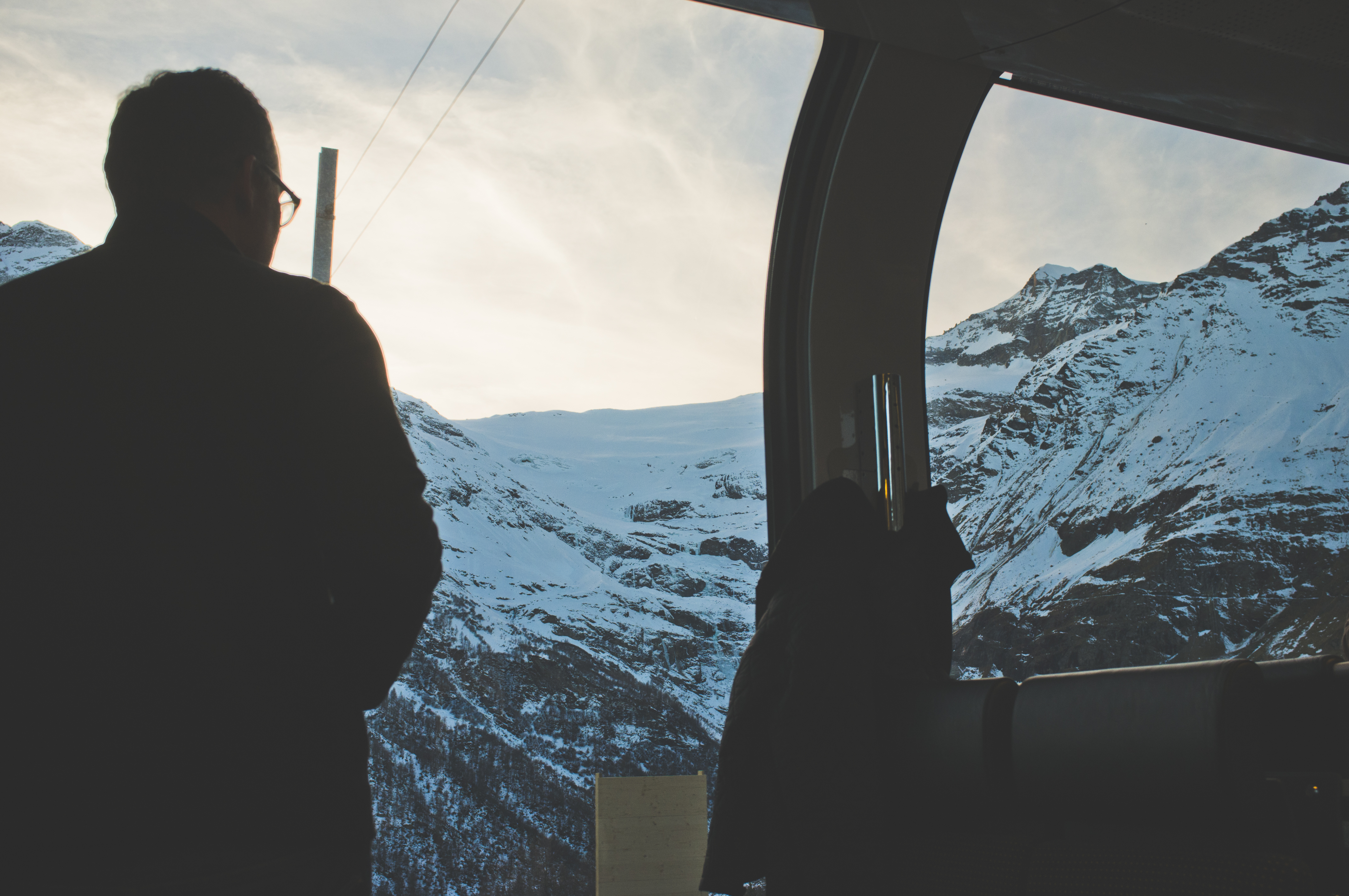 Dad silhouetted in profile looking out a panoramic train window toward snowy Swiss mountains.