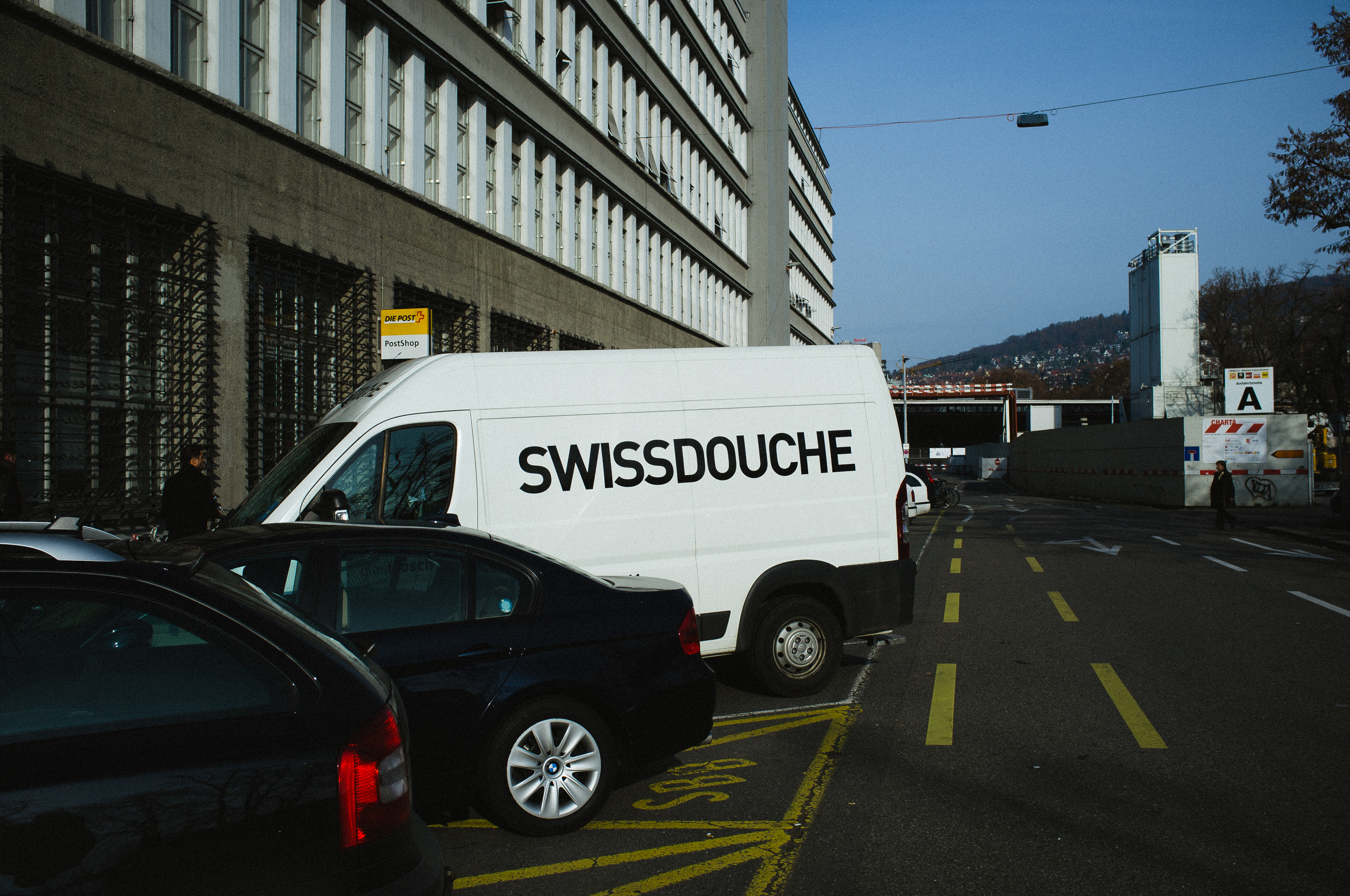 White cargo van with humorous 'SWISSDOUCHE' side lettering on a Zurich street outside apartments.