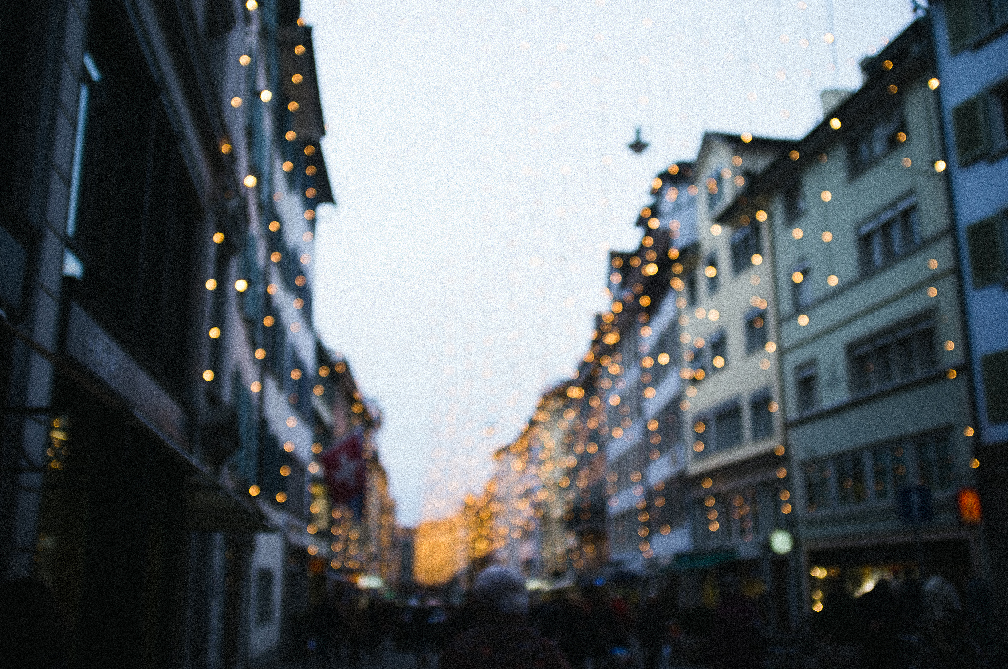Atmospheric bokeh blur of overhead holiday fairy lights glowing warmly above Zurich city street at twilight.