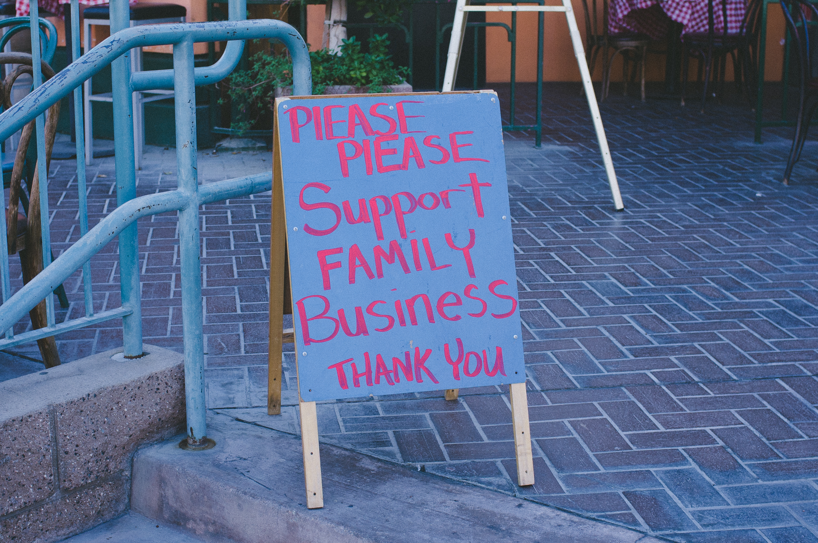 Sandwich board sign reading 'PLEASE PLEASE Support FAMILY Business THANK YOU' on a sidewalk.
