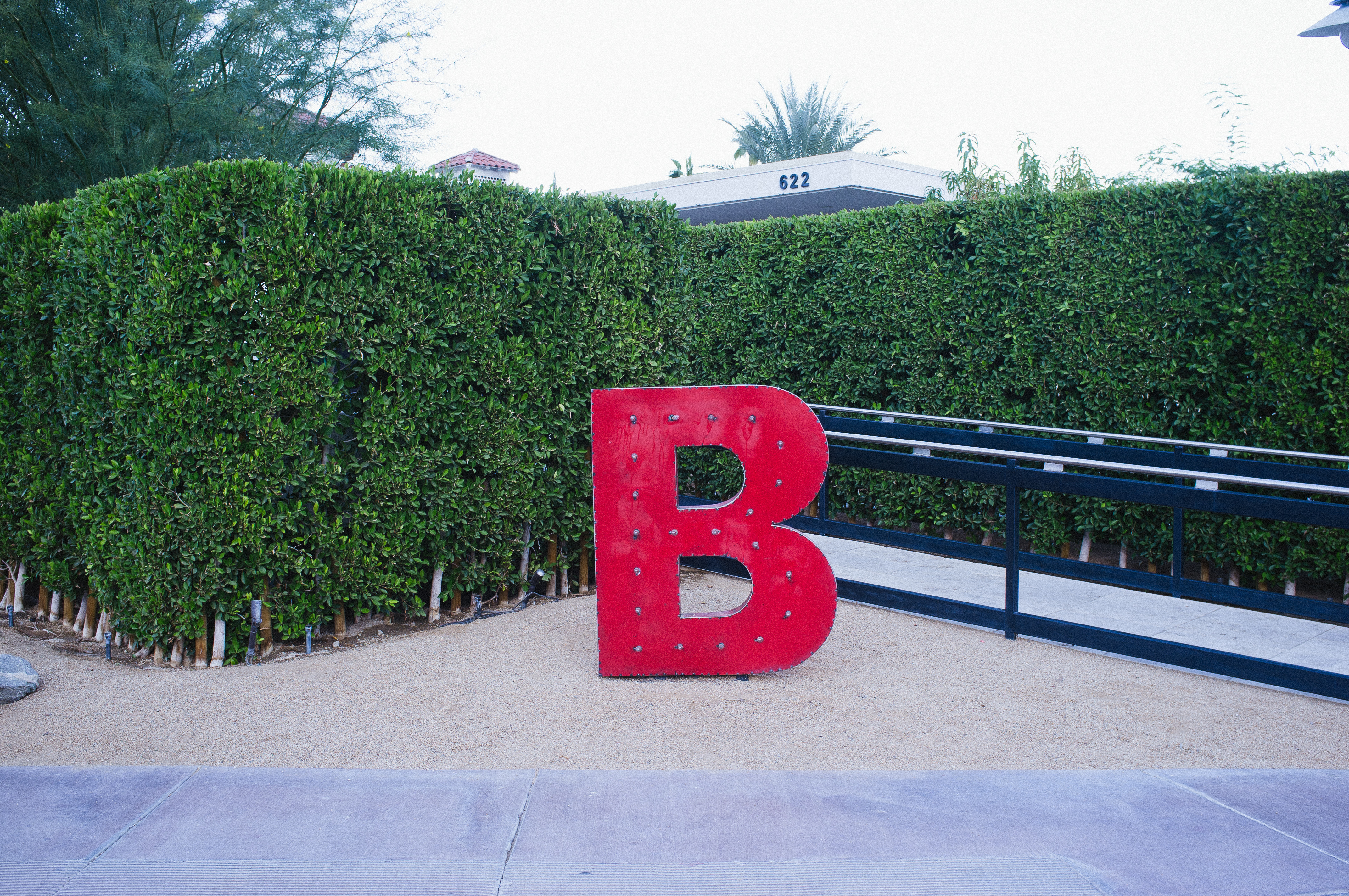 Lit red dimensional letter 'B' sign illuminated in front of green hedges outside 622 building in Palm Springs.