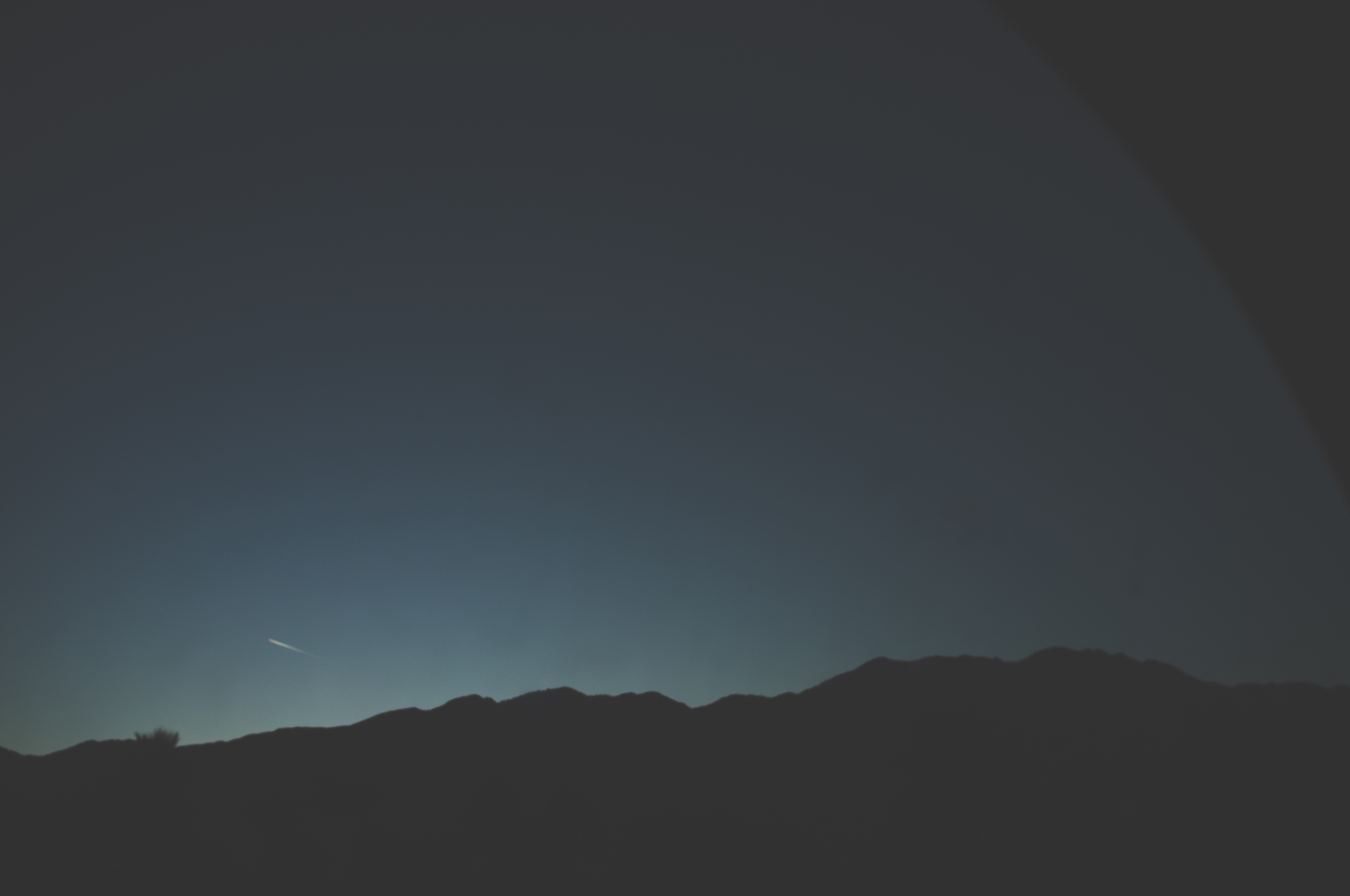 Airplane contrail illuminated by sunset in twilight sky above desert mountains in Palm Springs.