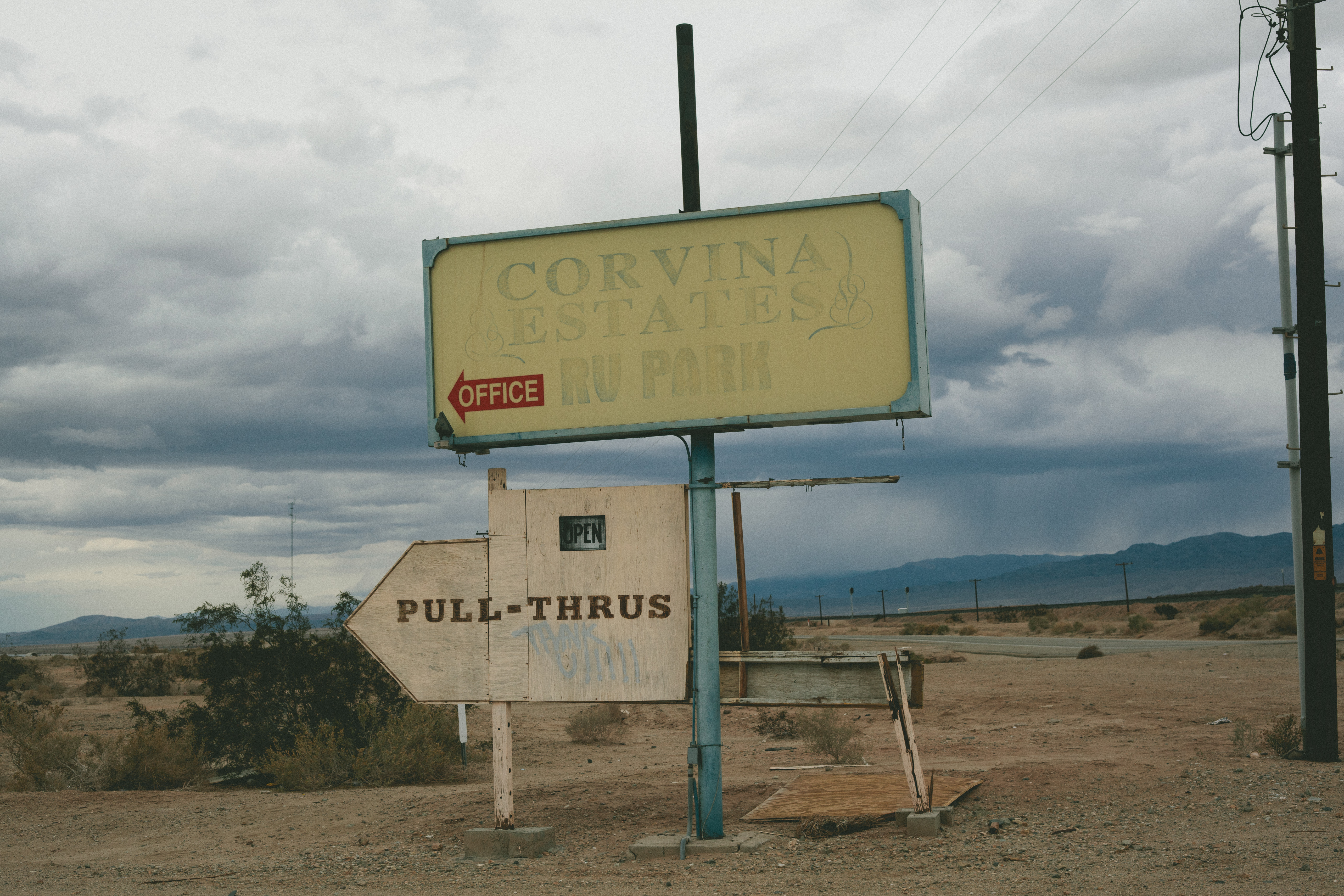 Faded vintage metal road sign in the desert announcing 'CORVINA ESTATES RV PARK' and mobile homes.