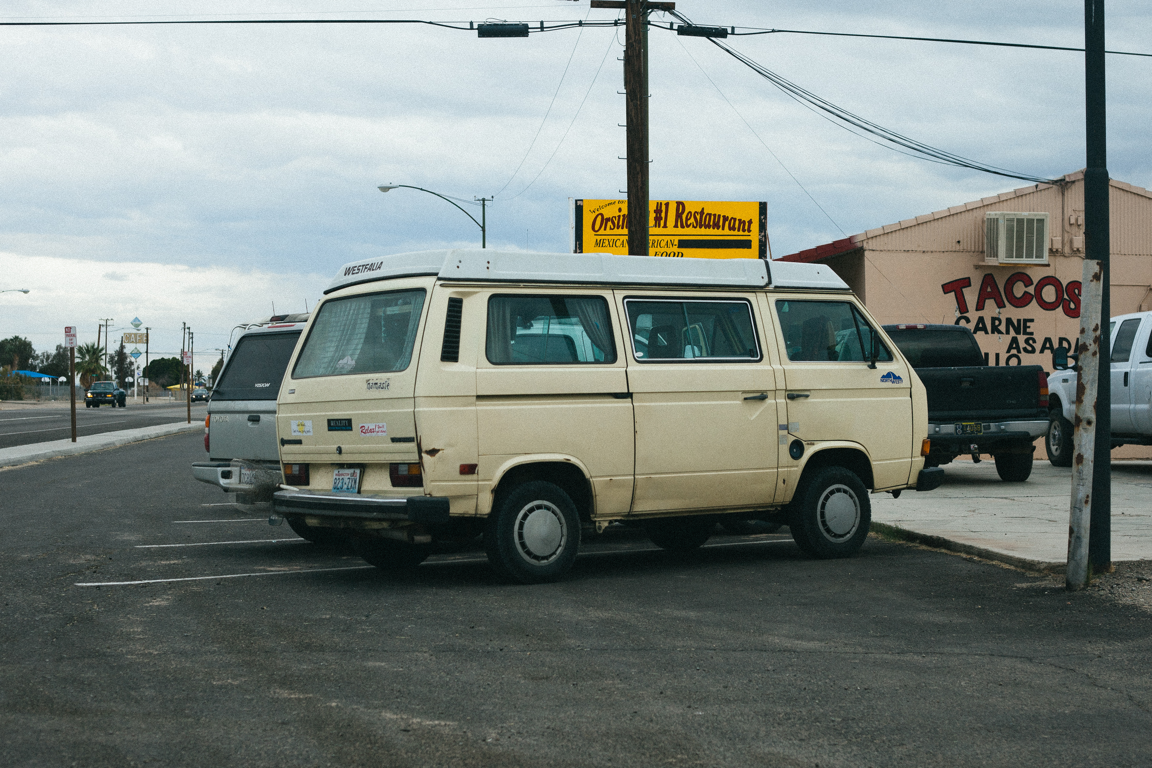 Cream Volkswagen Westfalia camper van parked in an asphalt lot outside a Mexican restaurant.