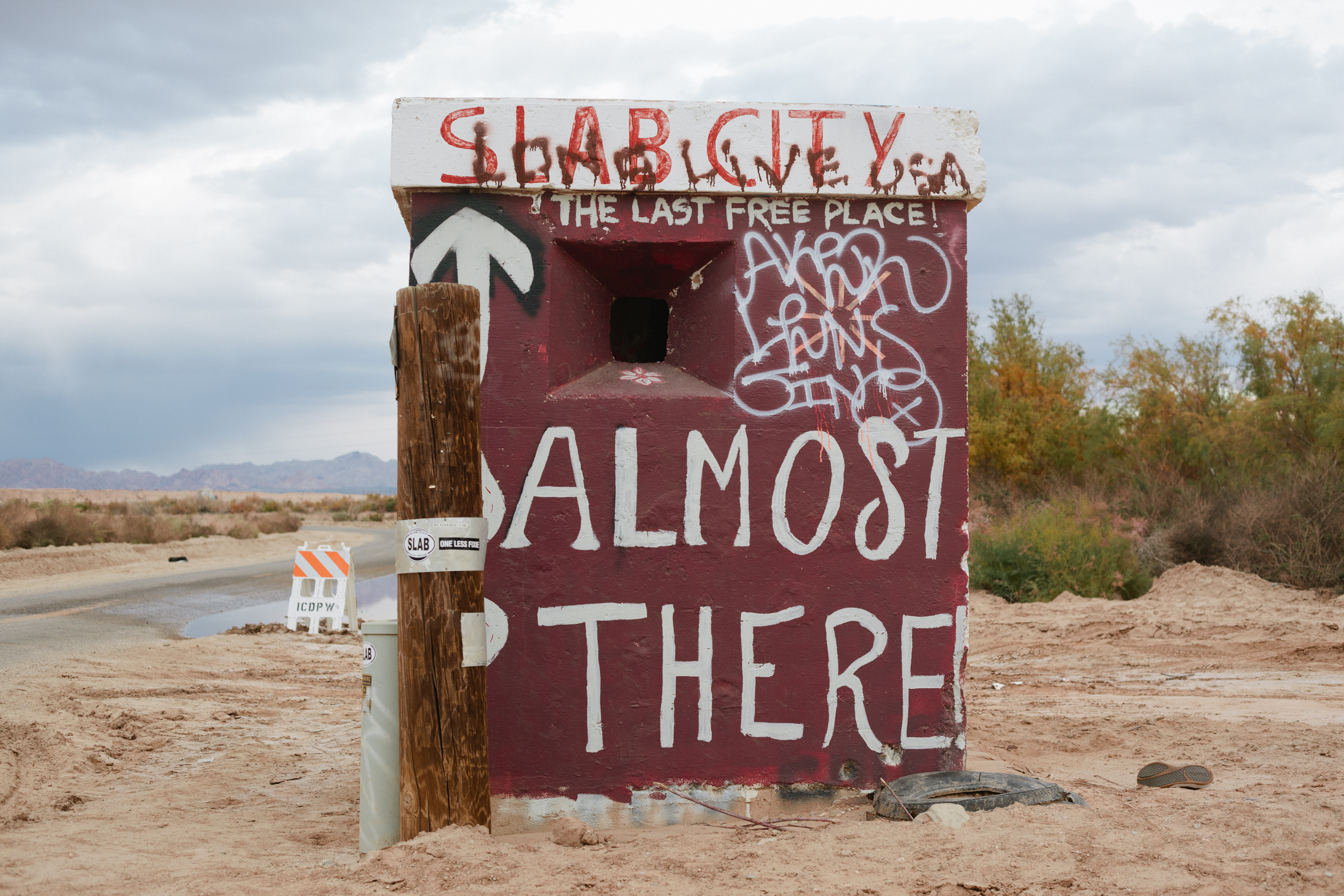 Concrete kiosk painted with 'ALMOST THERE!' and 'SLAB CITY THE LAST FREE PLACE!' in the desert.