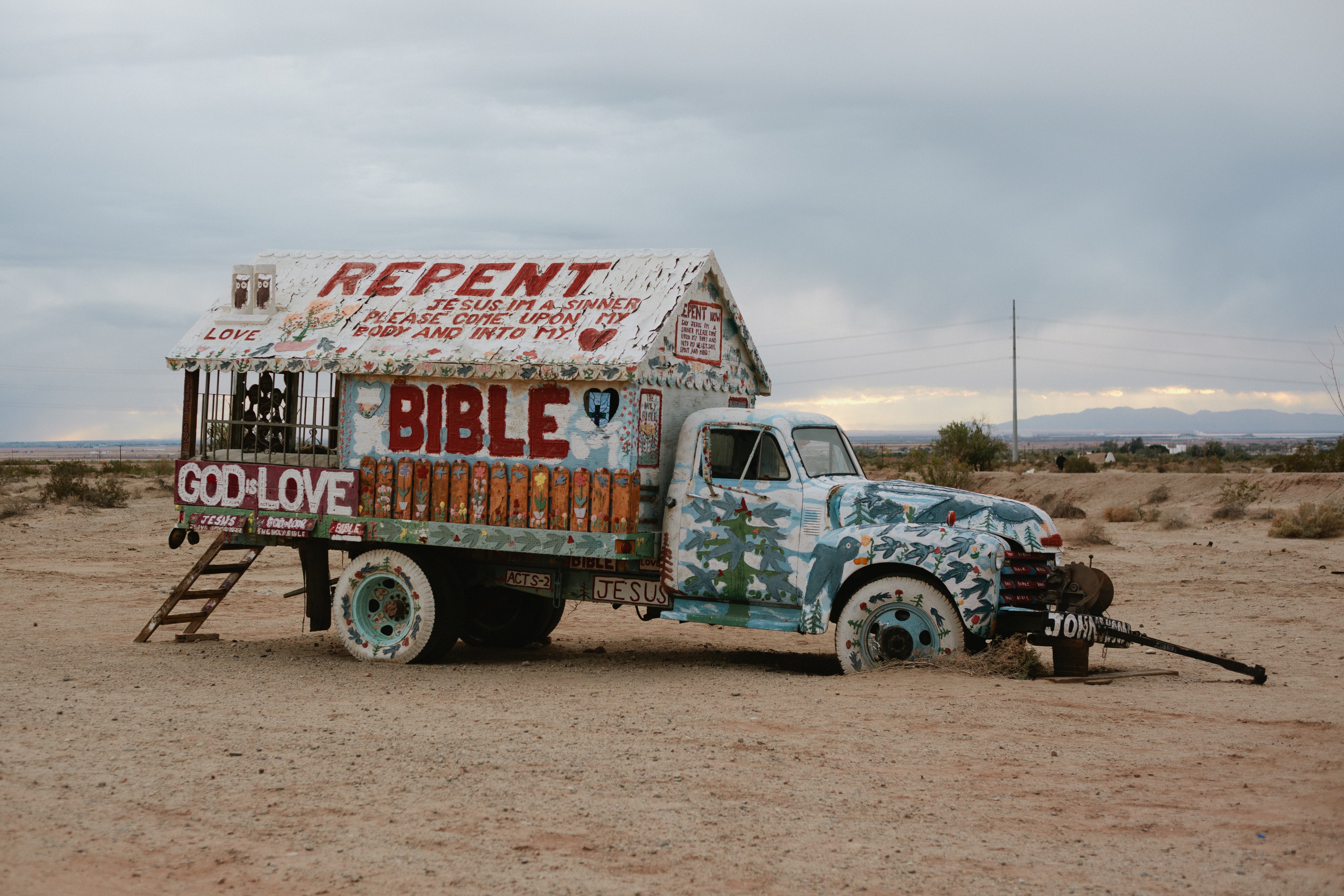 Truck covered in painted religious lettering reading 'GOD IS LOVE' and 'REPENT' at Salvation Mountain.