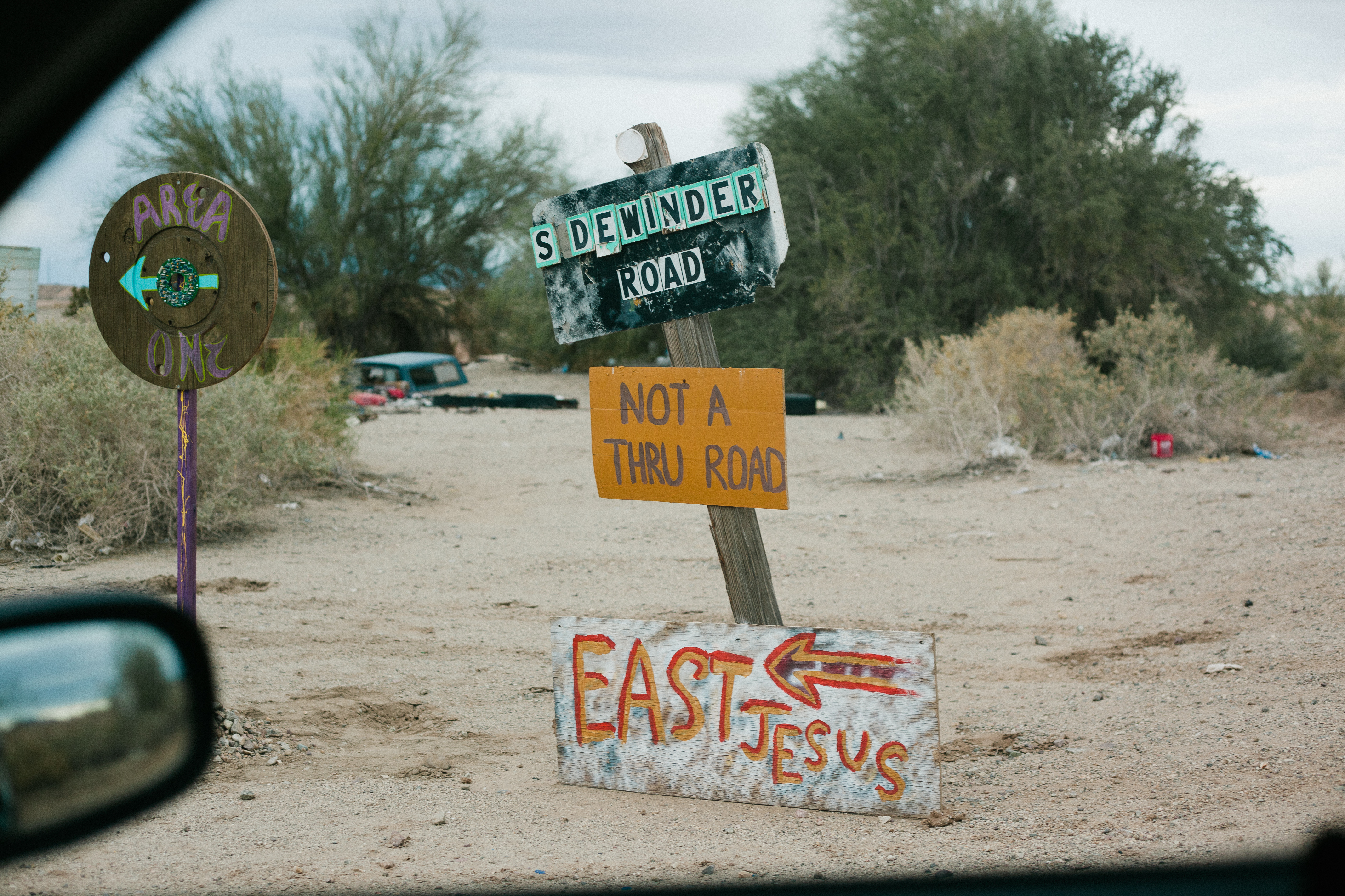 Hand-painted signs for 'SIDEWINDER ROAD', 'NOT A THRU ROAD', and an arrow toward 'EAST JESUS'.