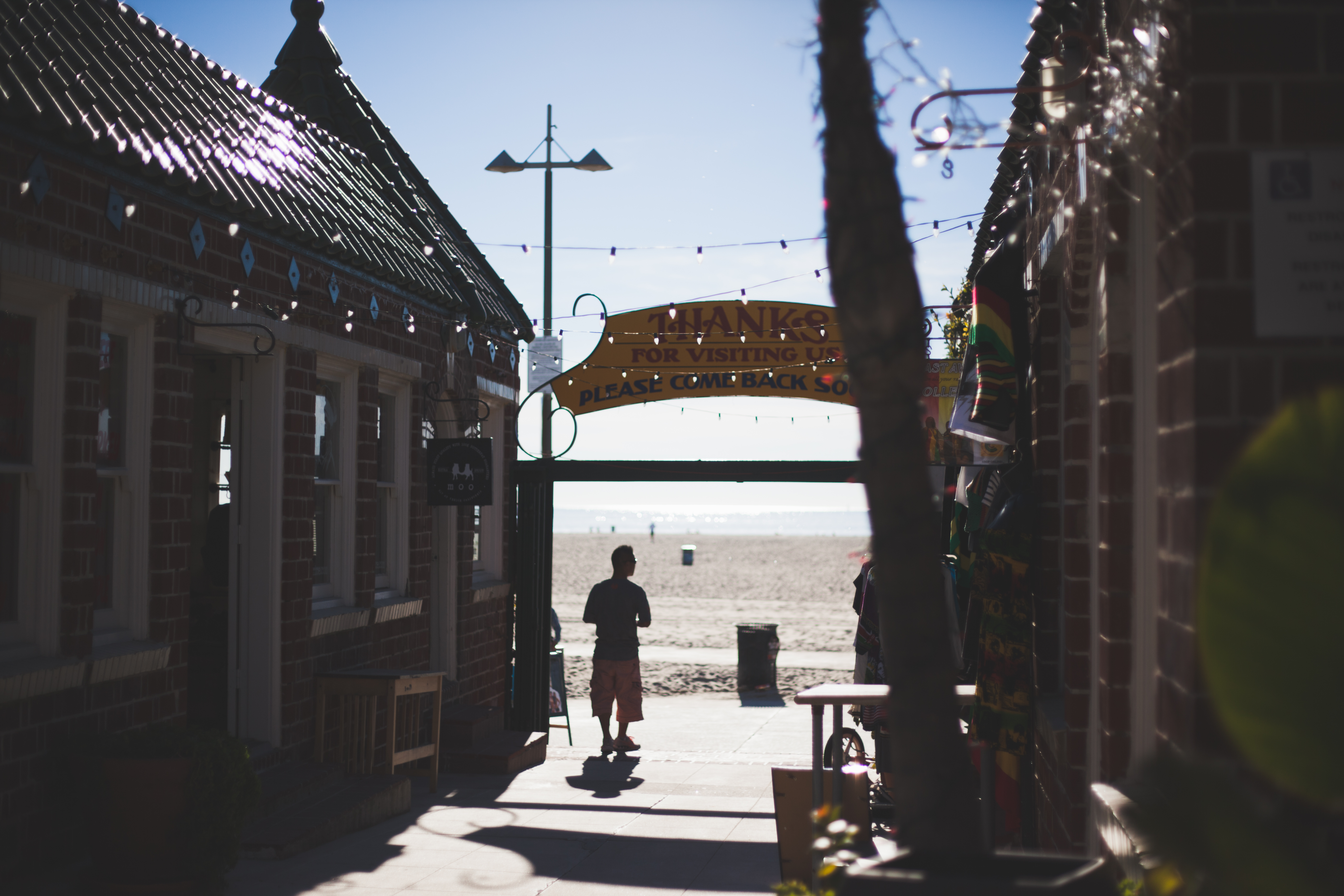 Brick walkway to Venice Beach under a sign reading 'THANKS FOR VISITING US PLEASE COME BACK SOON'.