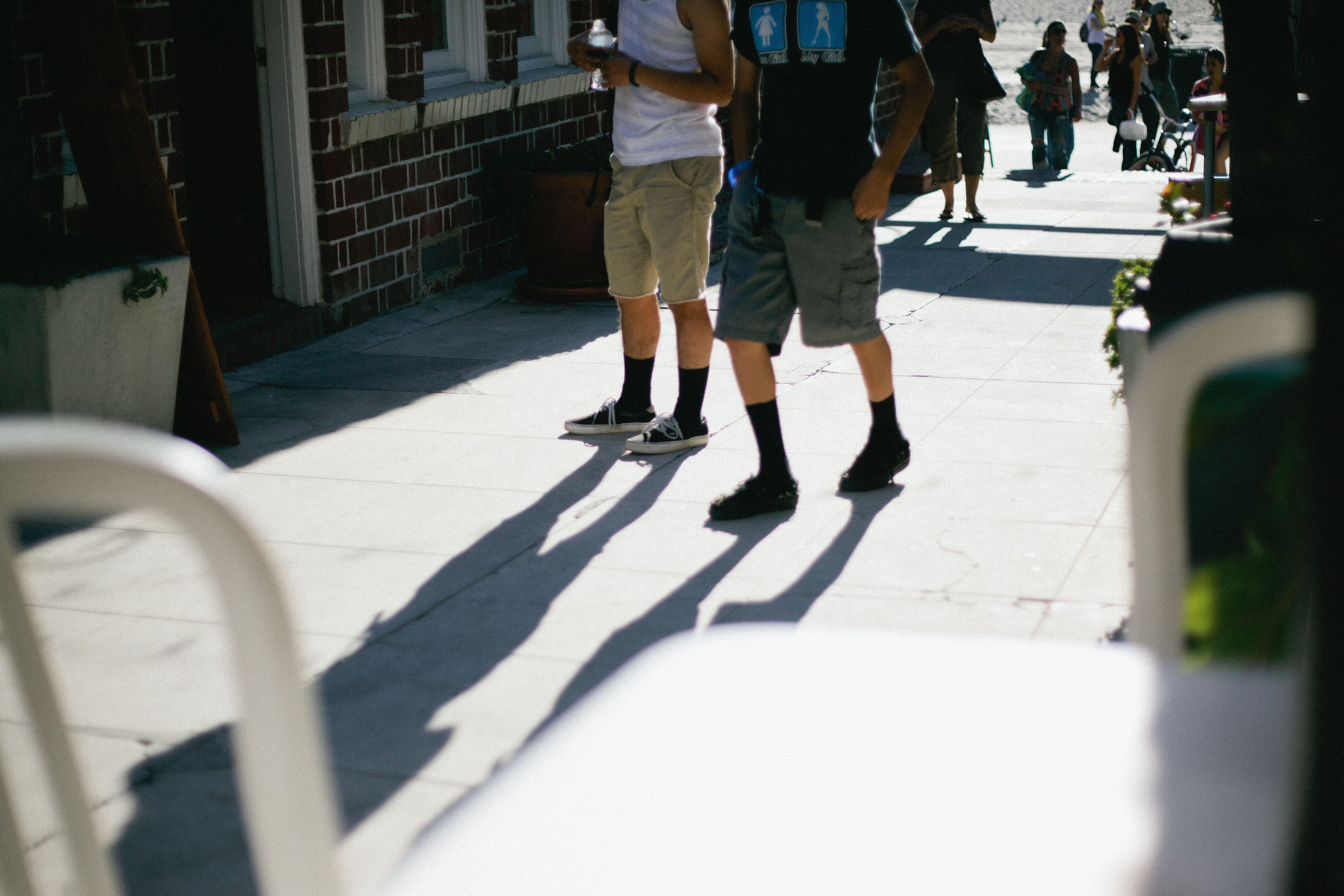 Two young men in shorts and black socks walking down a sunny sidewalk in Venice, California.