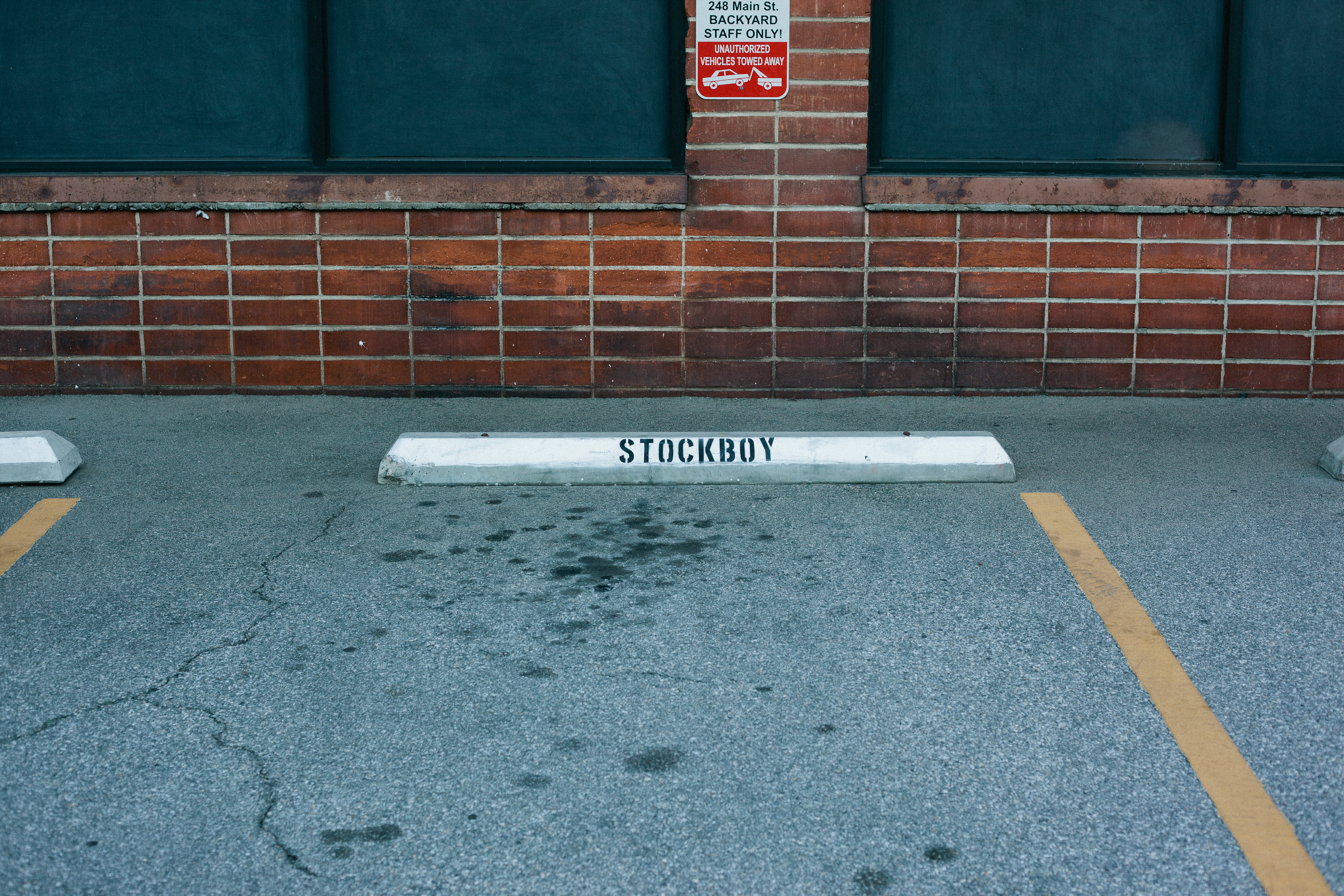 Concrete parking wheel stop stenciled with 'STOCKBOY' in black letters against a brick wall.