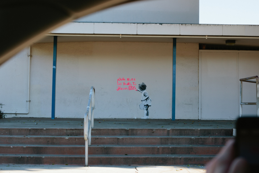 Street art stencil of a girl with text reading 'YOU\'RE NEVER TOO YOUNG TO dReaM BIG'.