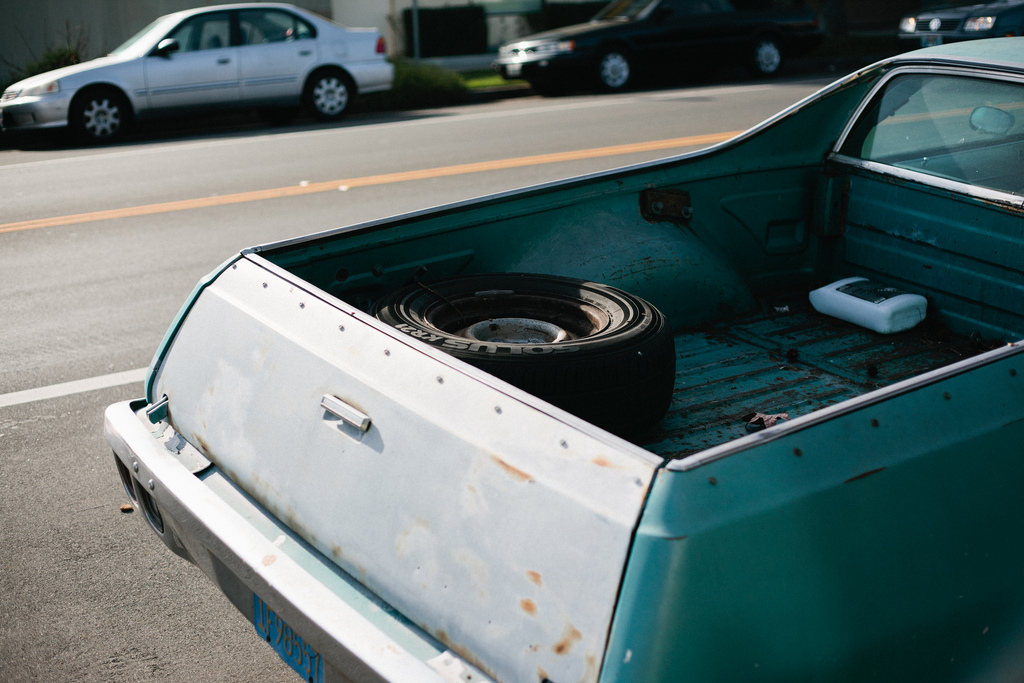 Weathered bed and tailgate of a teal Chevrolet El Camino carrying a spare tire.