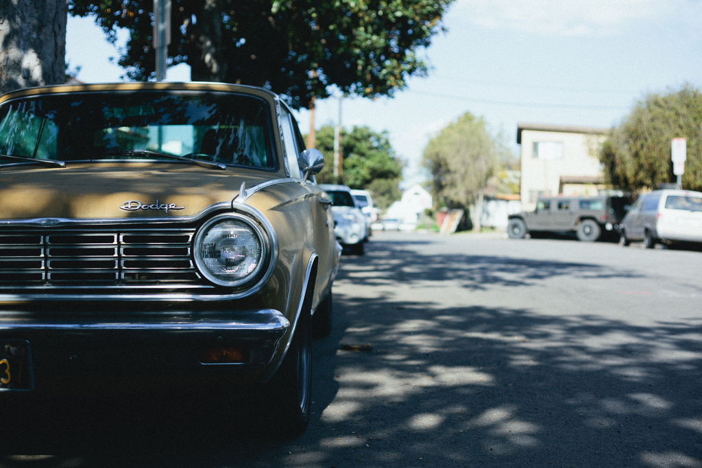 Vintage tan Dodge Dart showing its round headlight and chrome bumper on a quiet street.