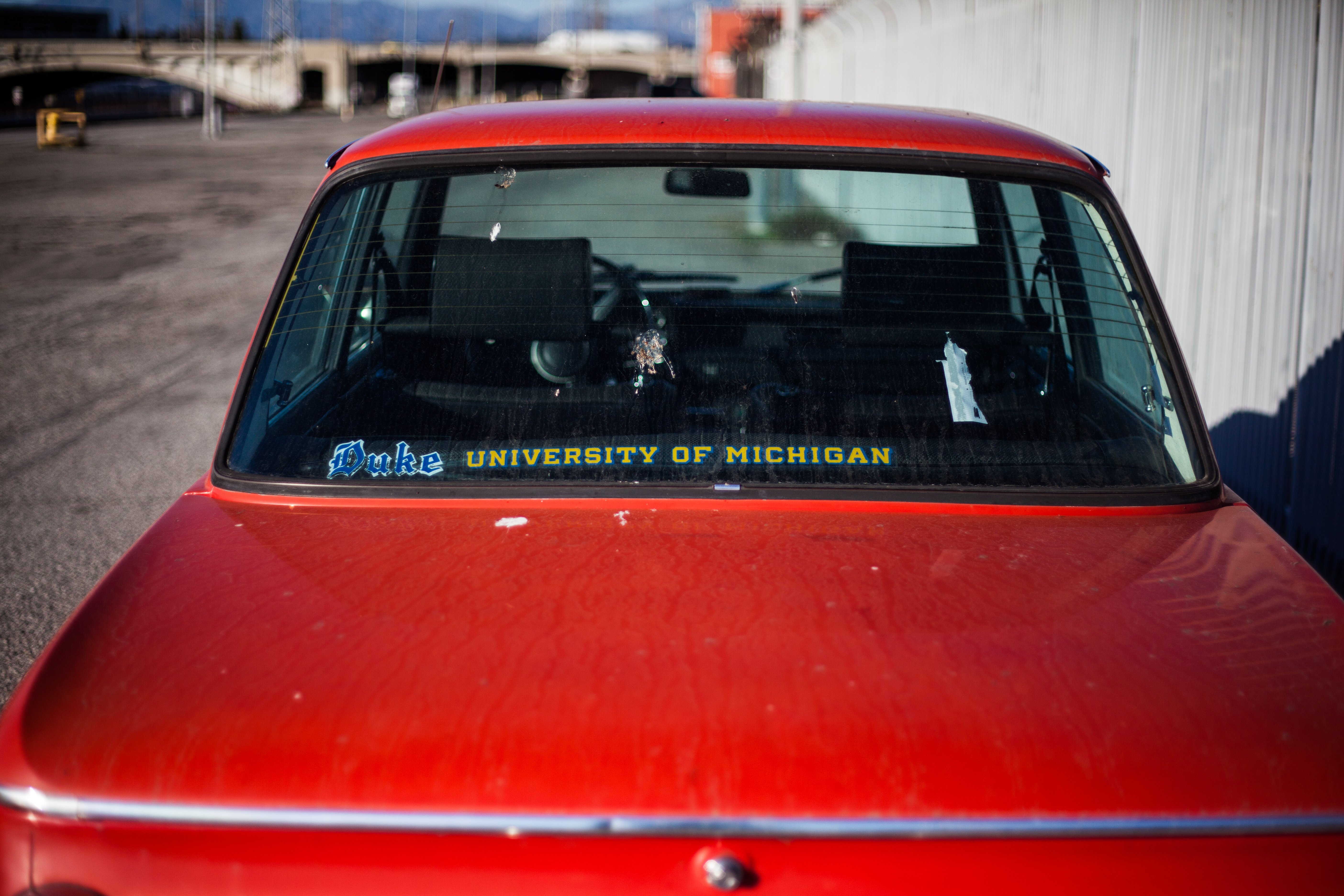 Dusty rear window of a red BMW coupe displaying Duke and University of Michigan decals.