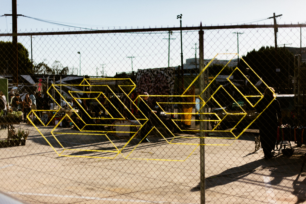 Bright yellow tape woven into a chain-link fence forming a geometric pattern outdoors.