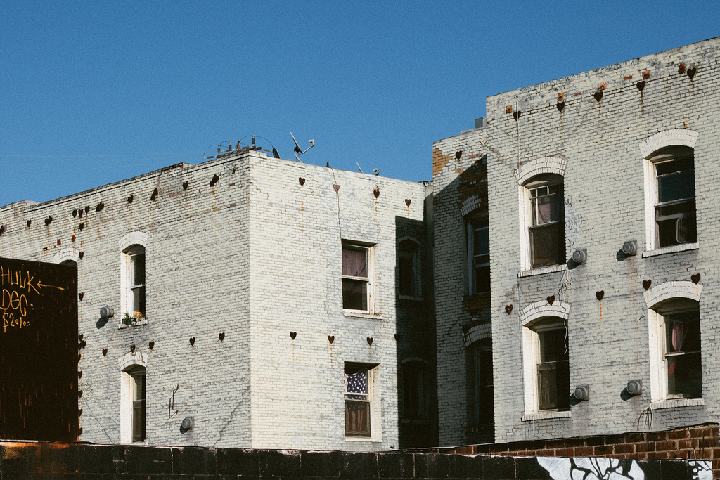 Whitewashed brick apartments with heart-shaped iron anchor plates and an American flag.