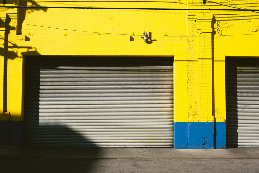 Yellow industrial brick building with a royal blue base and silver roll-up garage door.