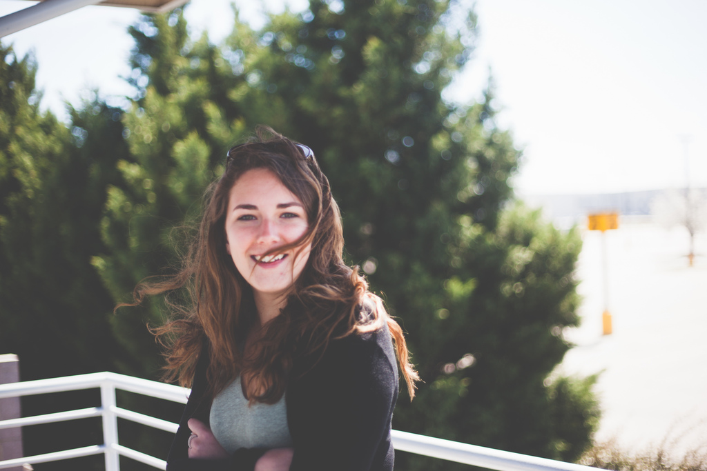 Smiling portrait of Maggie with windblown brown hair by a white balcony railing.