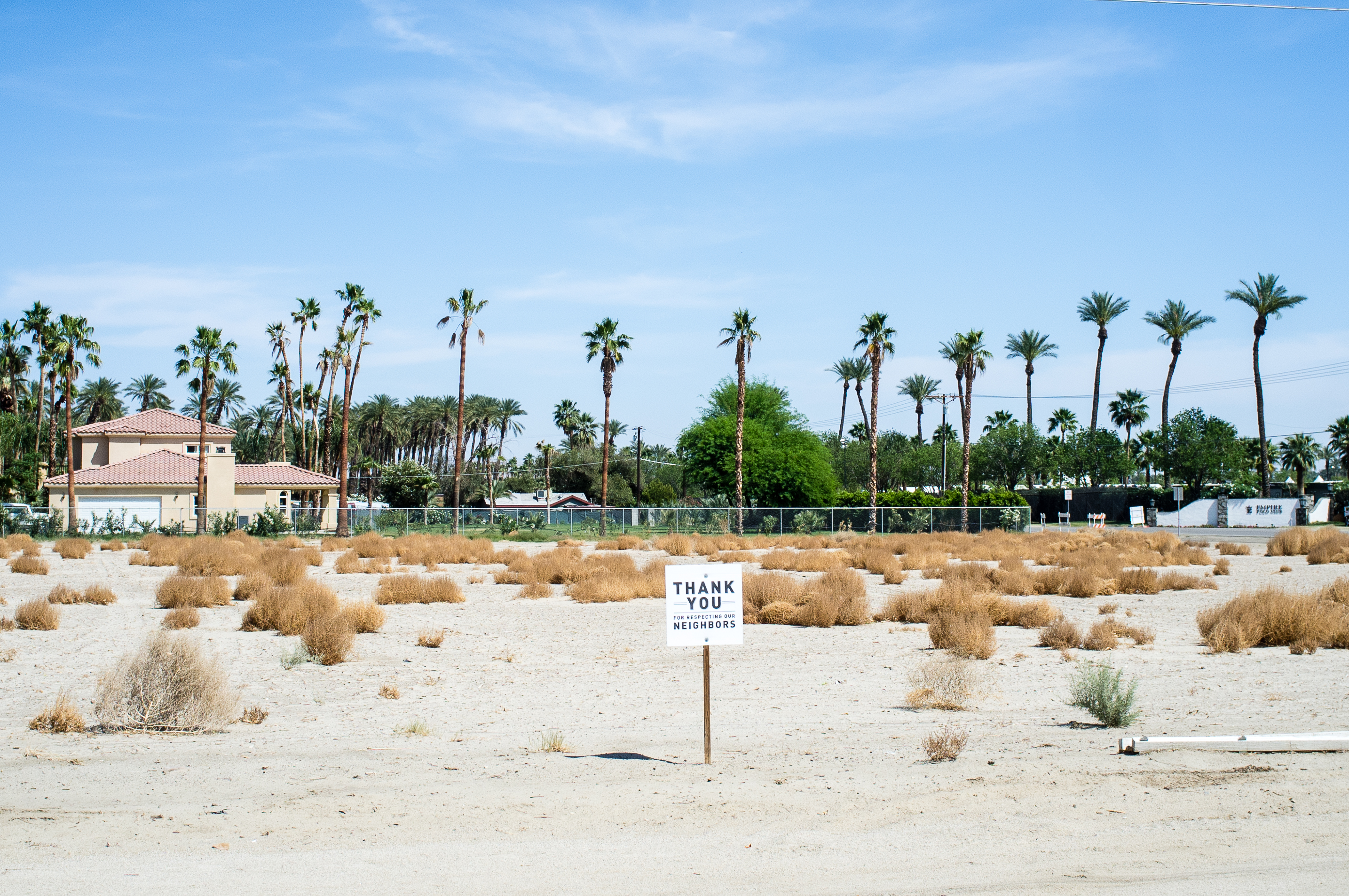 Sandy desert lot with tumbleweeds and a 'THANK YOU FOR RESPECTING OUR NEIGHBORS' sign in Coachella.