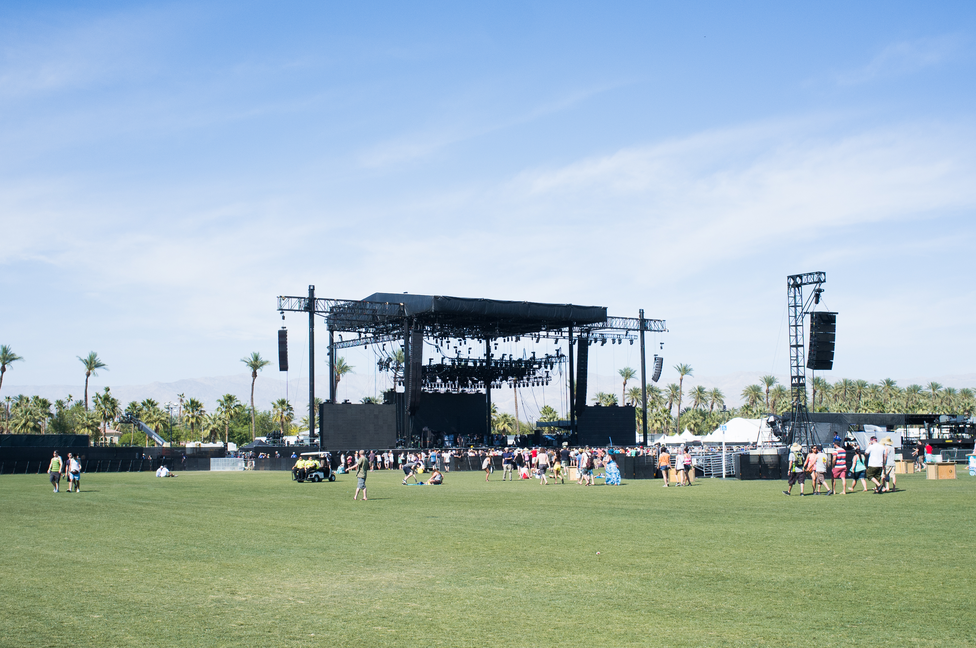 Green festival lawn leading toward the massive outdoor Coachella main stage rigging.