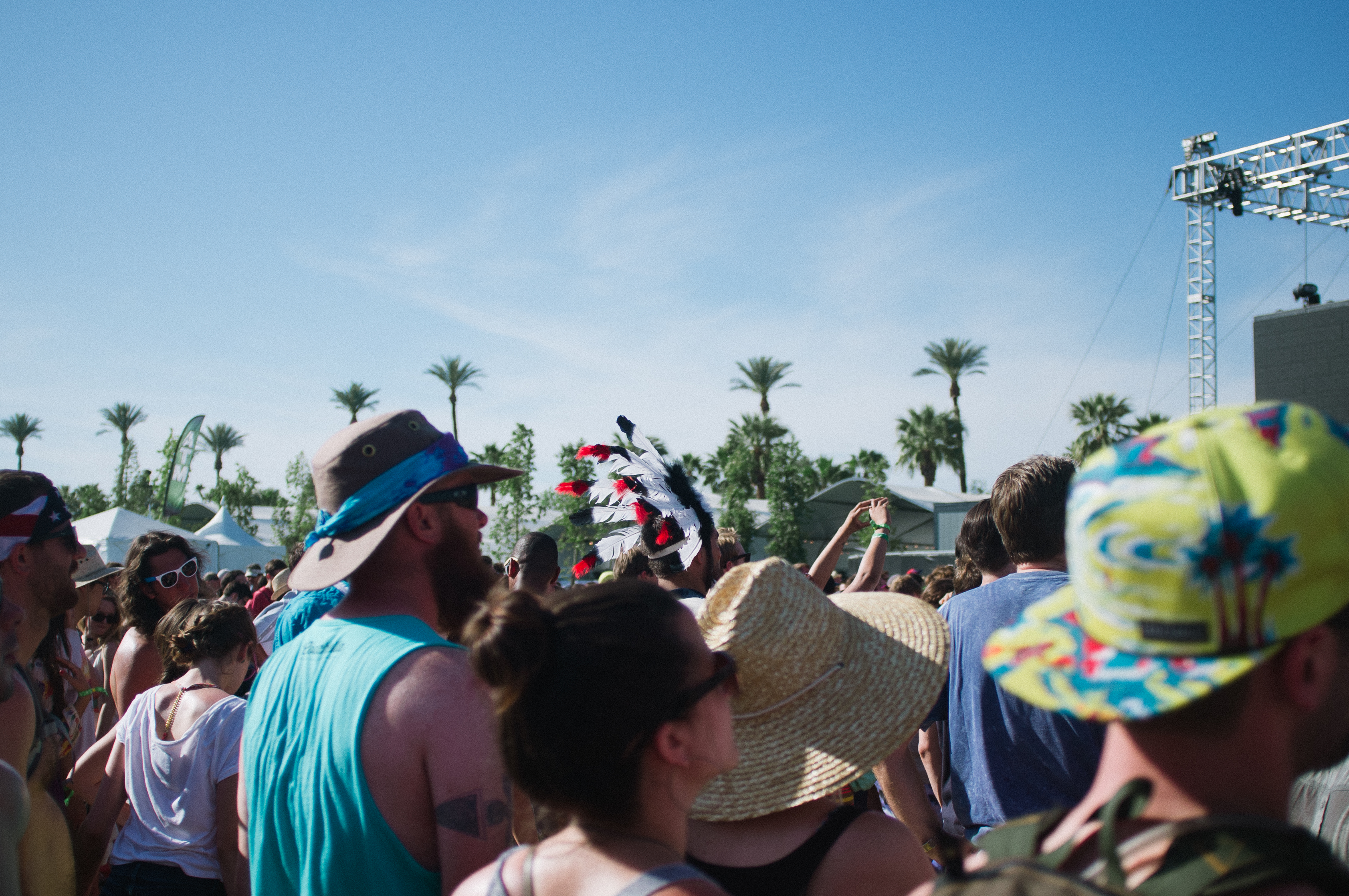 Festival crowd in hats and sunglasses watching an outdoor performance at Coachella.