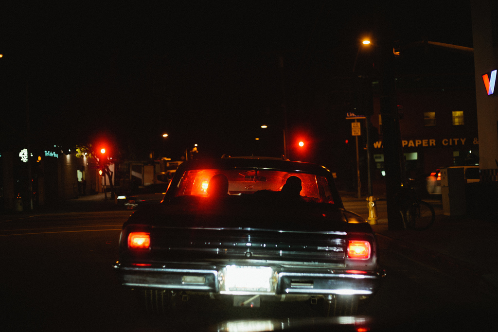 Glowing taillights and chrome bumper of an antique car stopped at a California intersection at night.