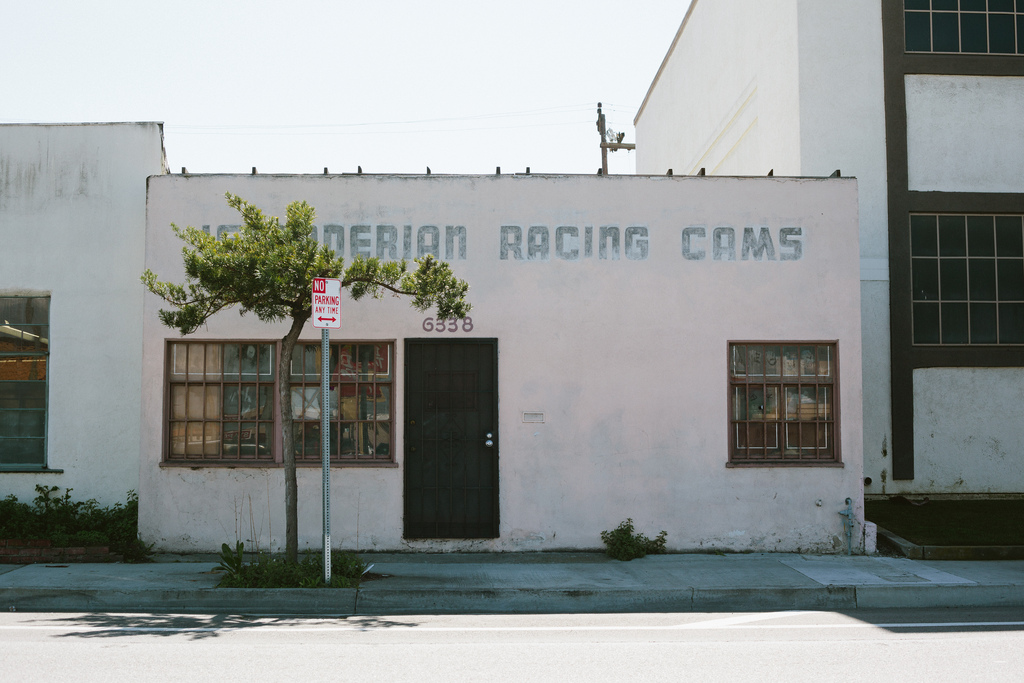 Faded pink facade of Iskenderian Racing Cams with barred windows and parking sign in Culver City.