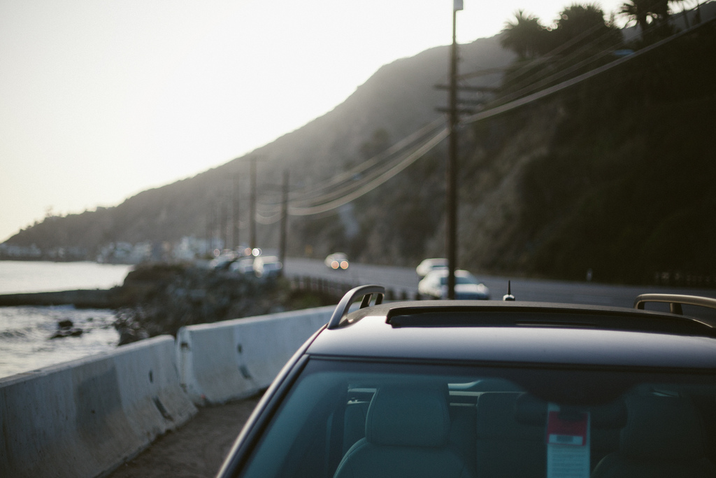 View over the roof of a parked car looking down the Pacific Coast Highway bordered by concrete barriers and seaside bluffs at dusk in California, shot with a Canon 5D Mark II.