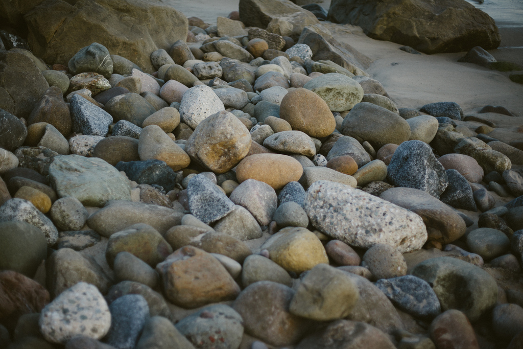Assortment of smooth, rounded beach stones and cobbles scattered across the sand along a California beach.