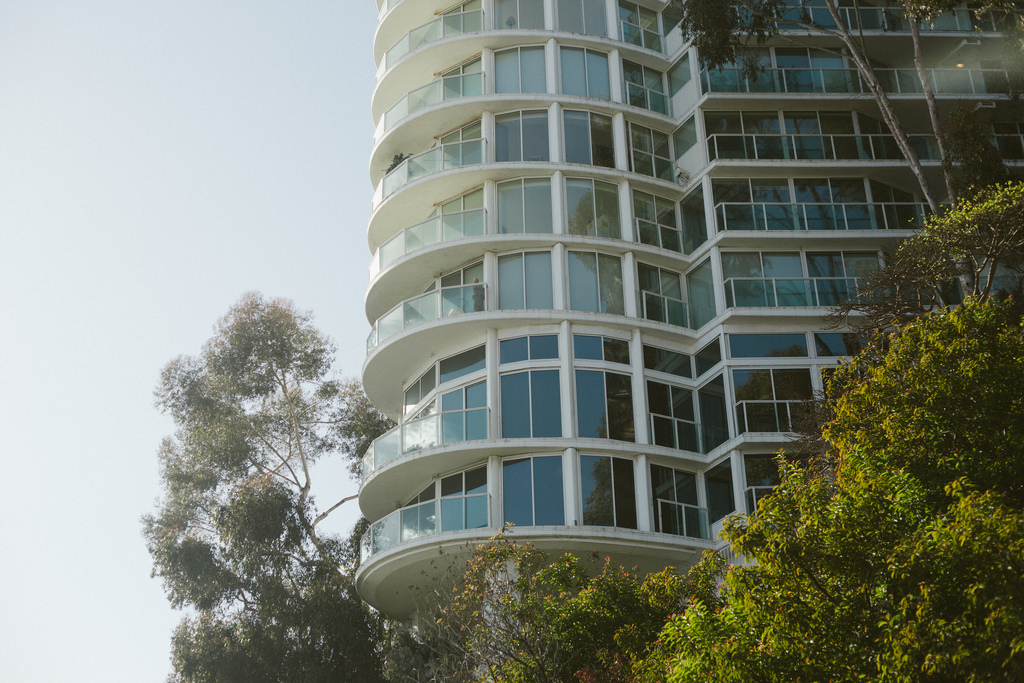Curved balconies of a white high-rise rising above eucalyptus trees and hillside foliage in California.
