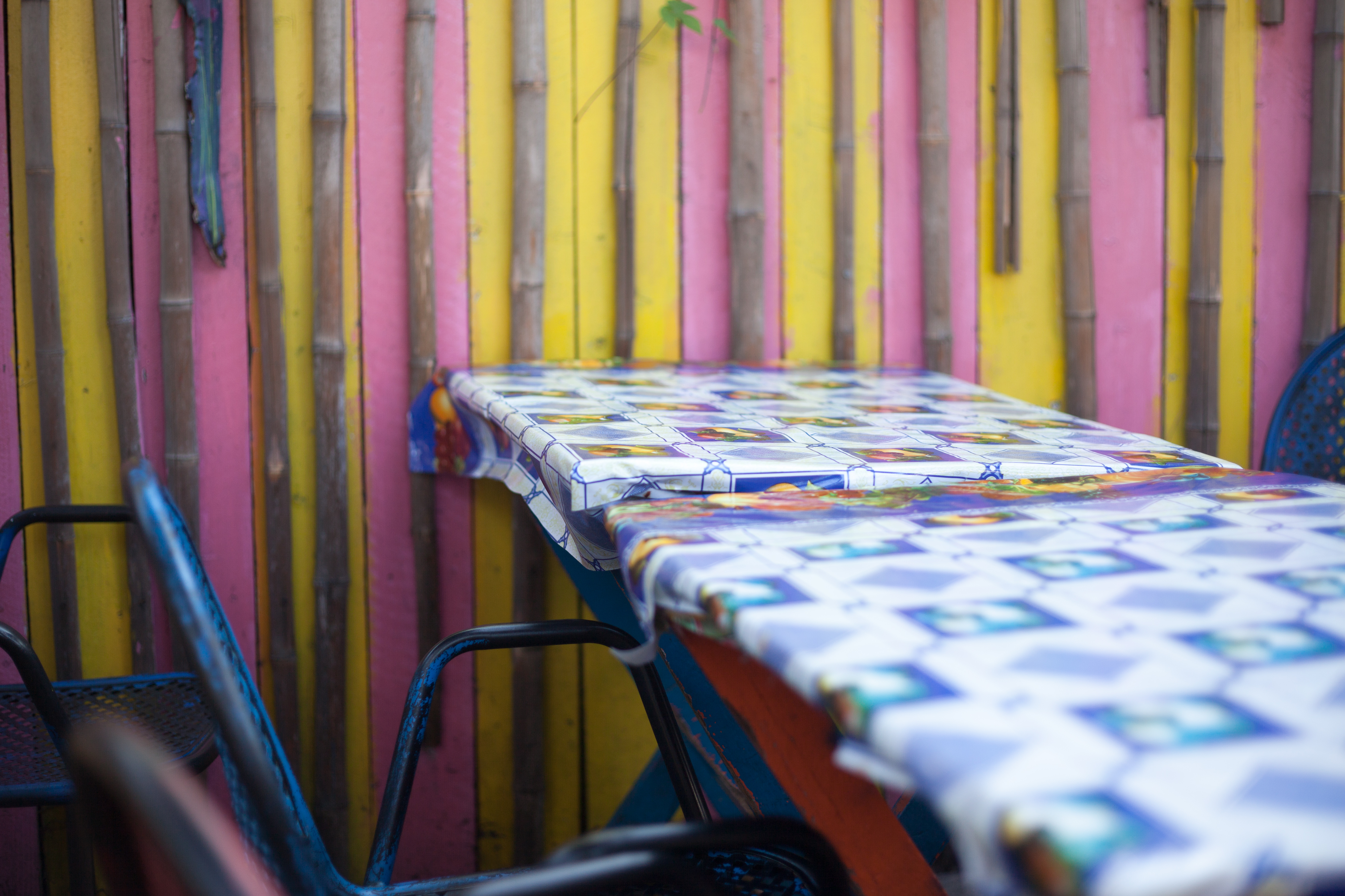 Patio dining table in a blue patterned cloth against a vibrant yellow and pink striped wall.