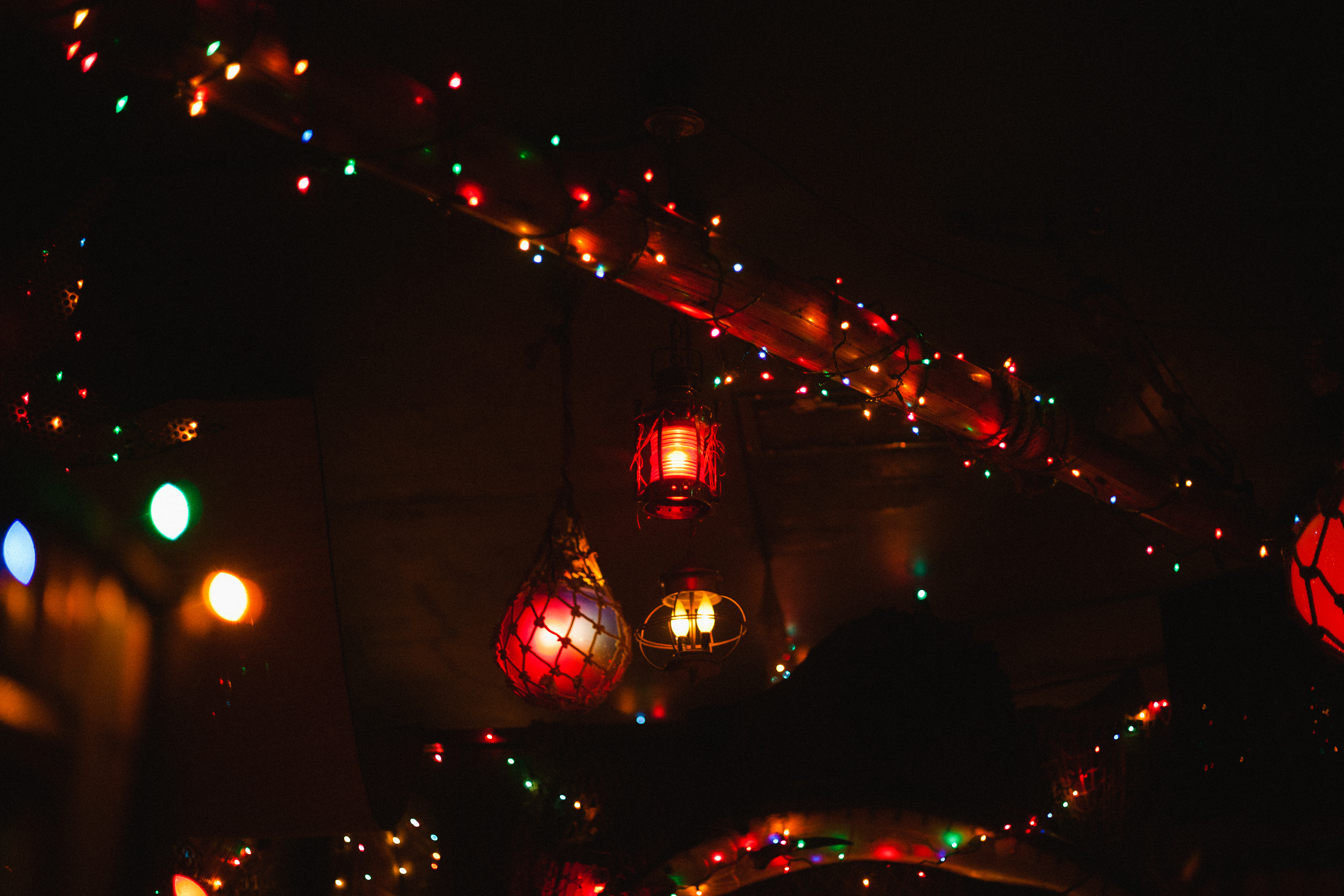 Netted glass buoy lights, lanterns, and strings of colorful fairy lights hanging from a ceiling.