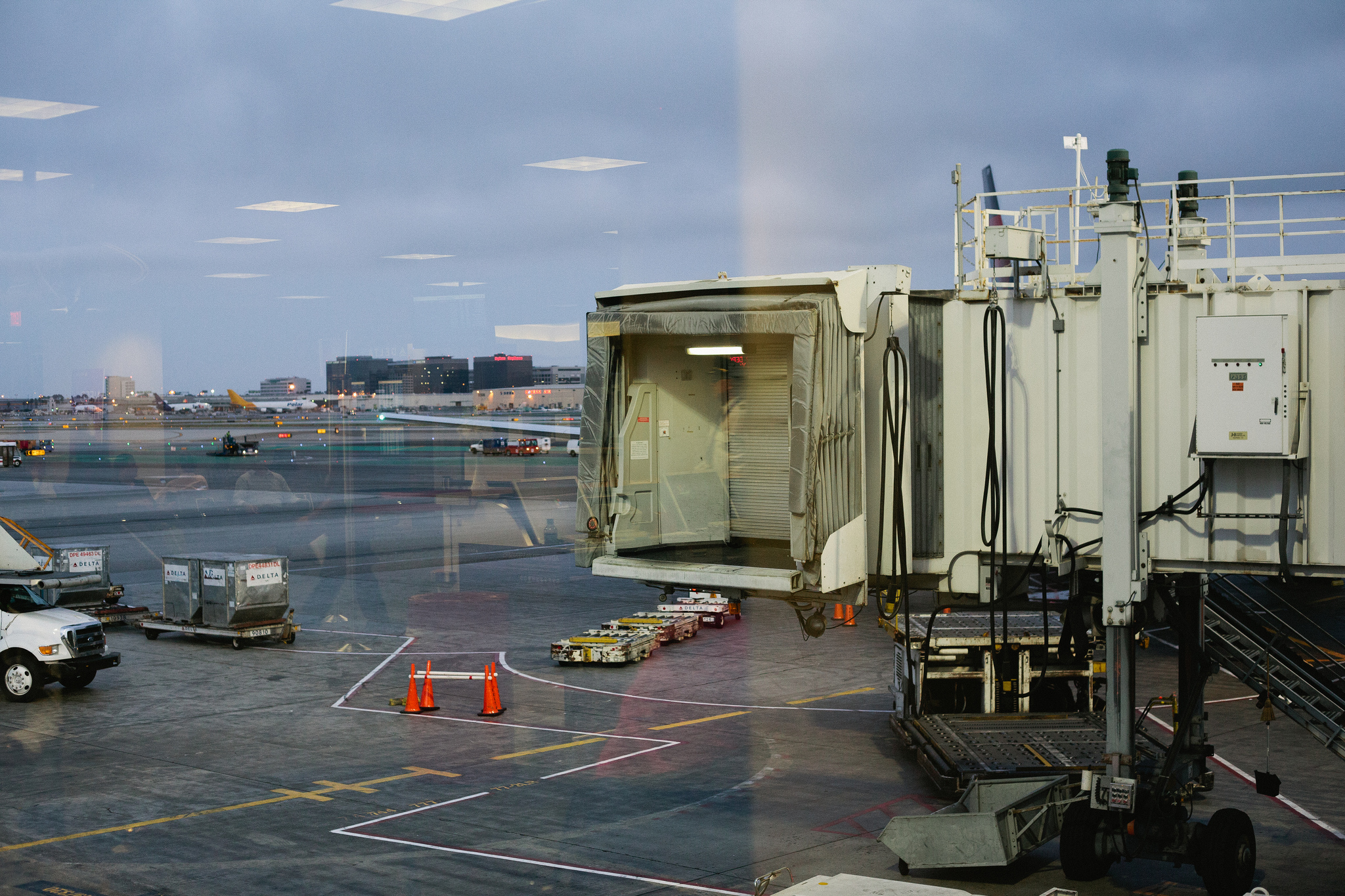 Airport tarmac at dusk with an open jet bridge walkway and Delta baggage containers outside.