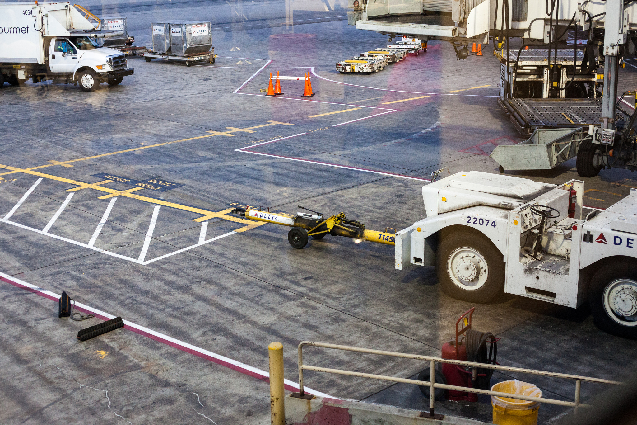 Airport tarmac apron with a Delta pushback tug connected to a yellow aircraft towbar.